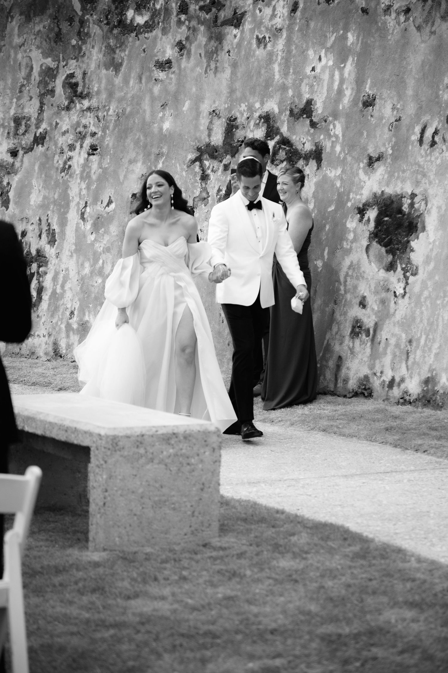 Wedding party poses along a weathered stone wall in black and white photography.