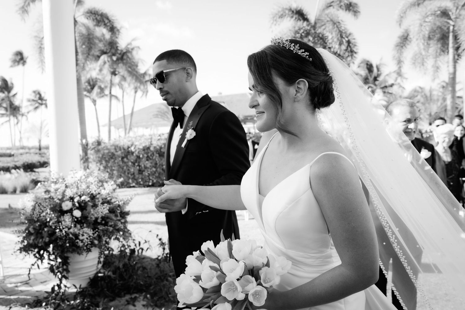 Two people share a romantic moment in black and white surrounded by palm trees and sunlight.