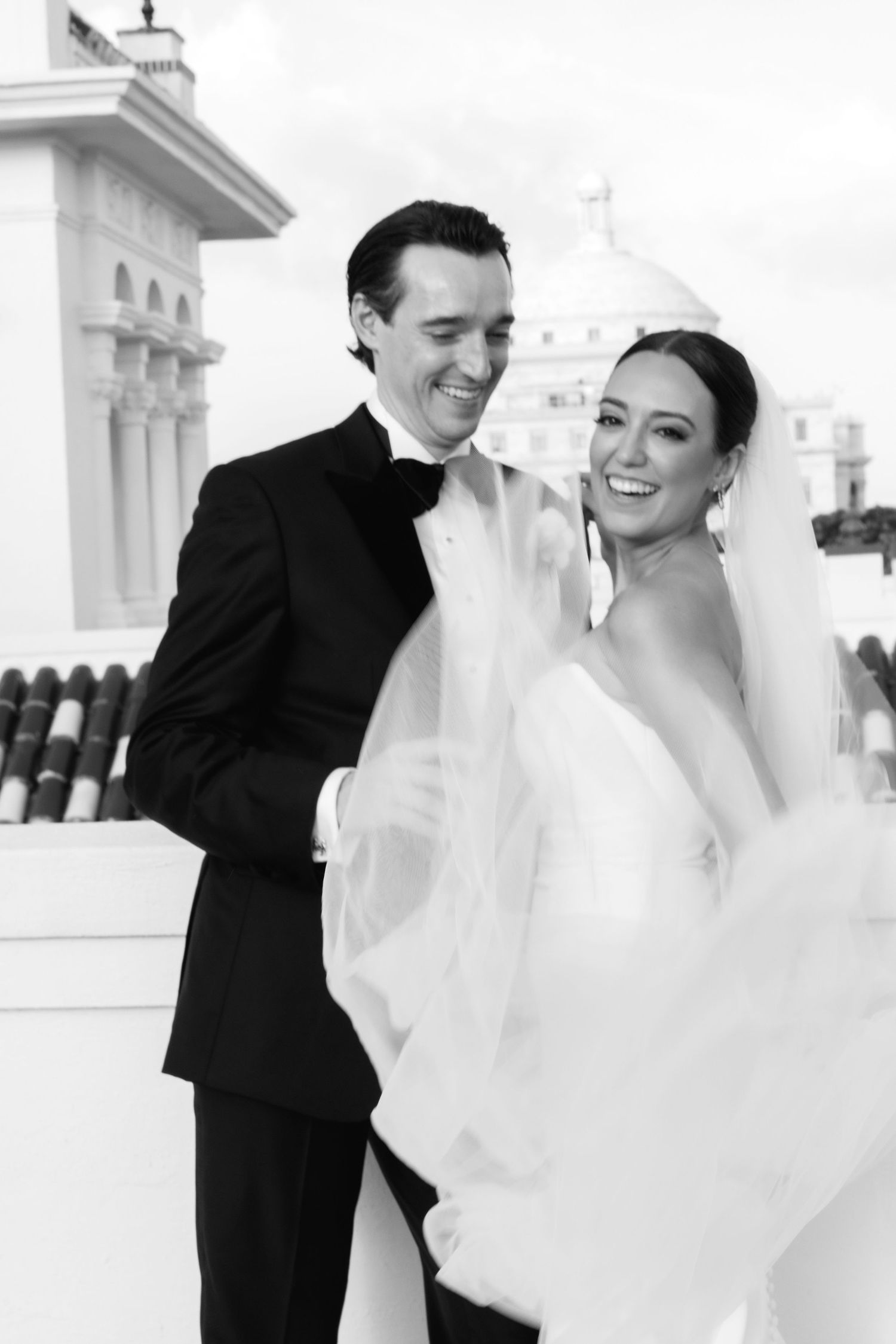 Wedding couple embrace and dance outdoors near white classic architecture on a bright sunny day.