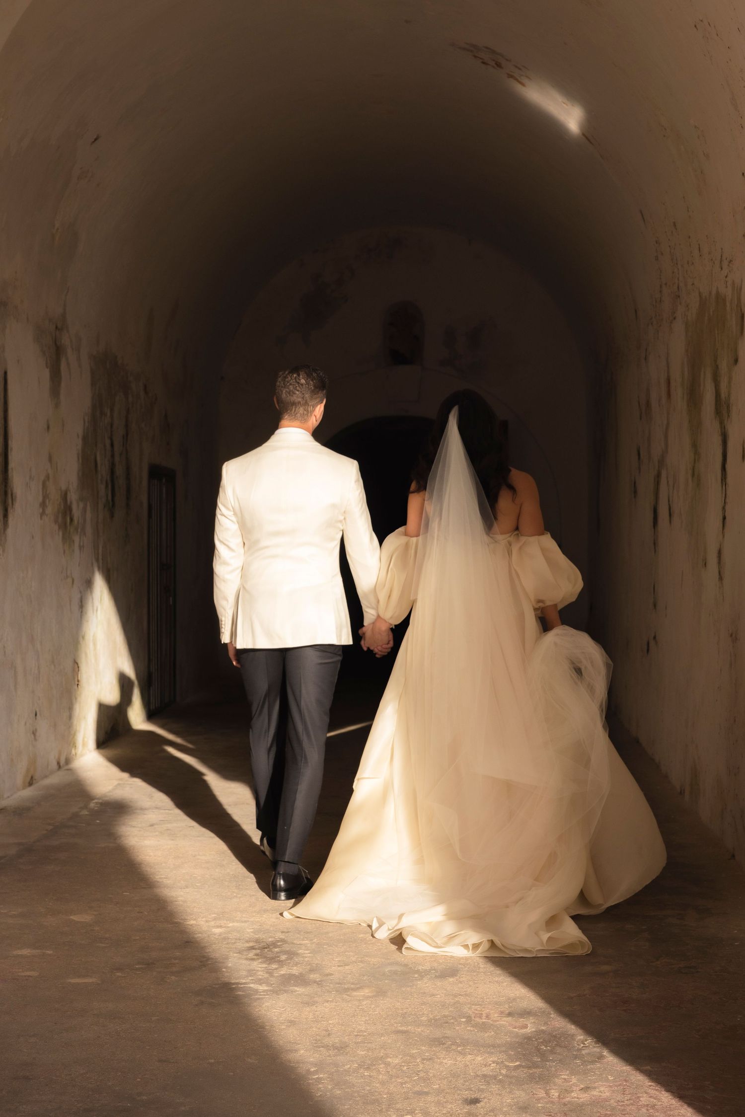 Dramatic shadows follow couple through dark tunnel in wedding attire.