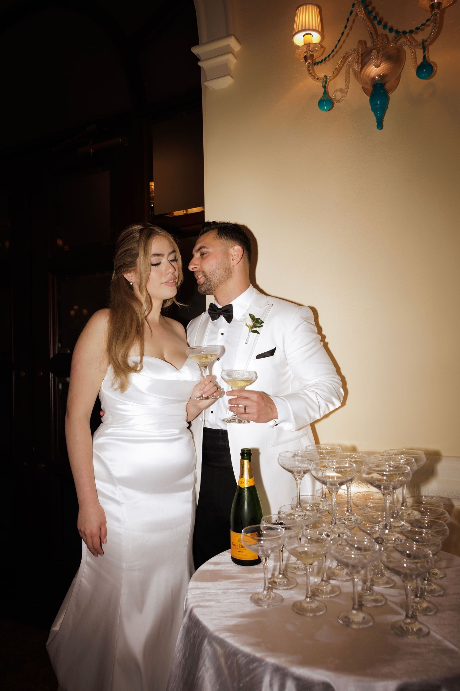 Couple in wedding attire sharing champagne beside a table with elegant crystal glasses at a reception.