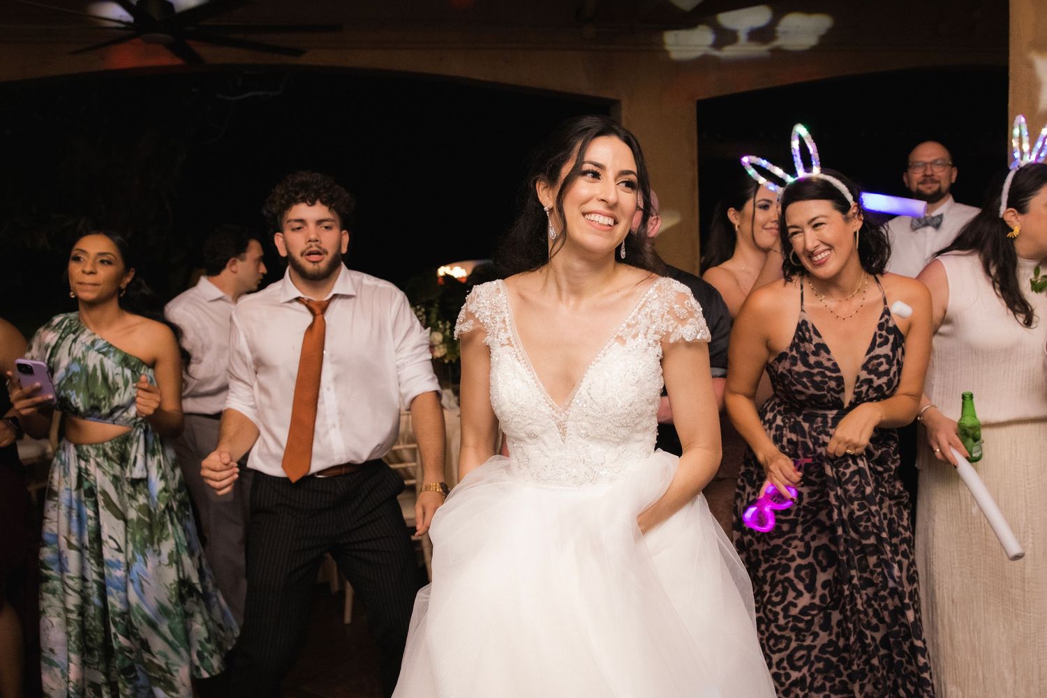 Wedding guests dancing together on a dance floor during a celebration reception with festive lighting.