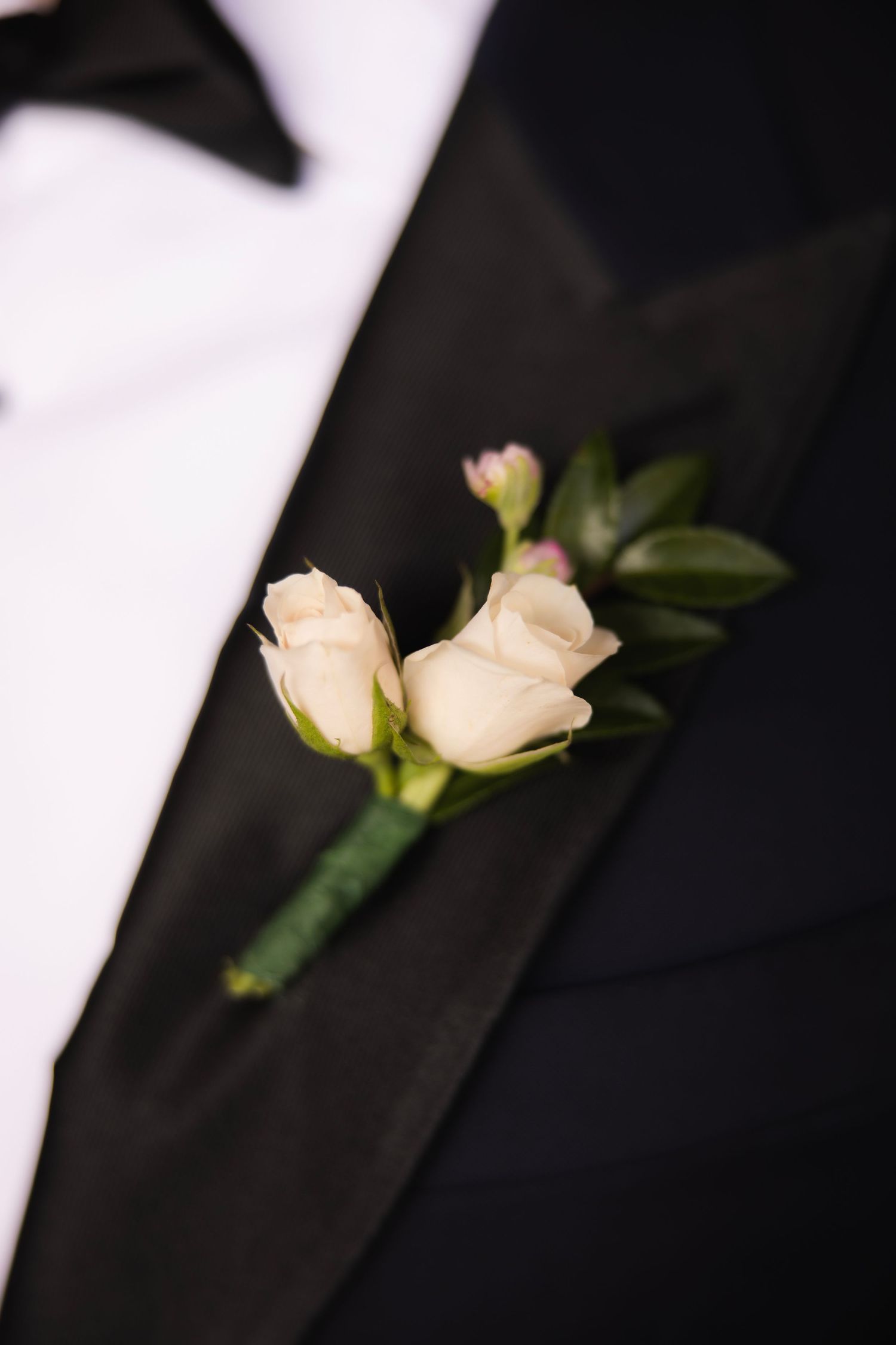 Elegant white rose boutonnieres pinned on black tuxedo lapels.