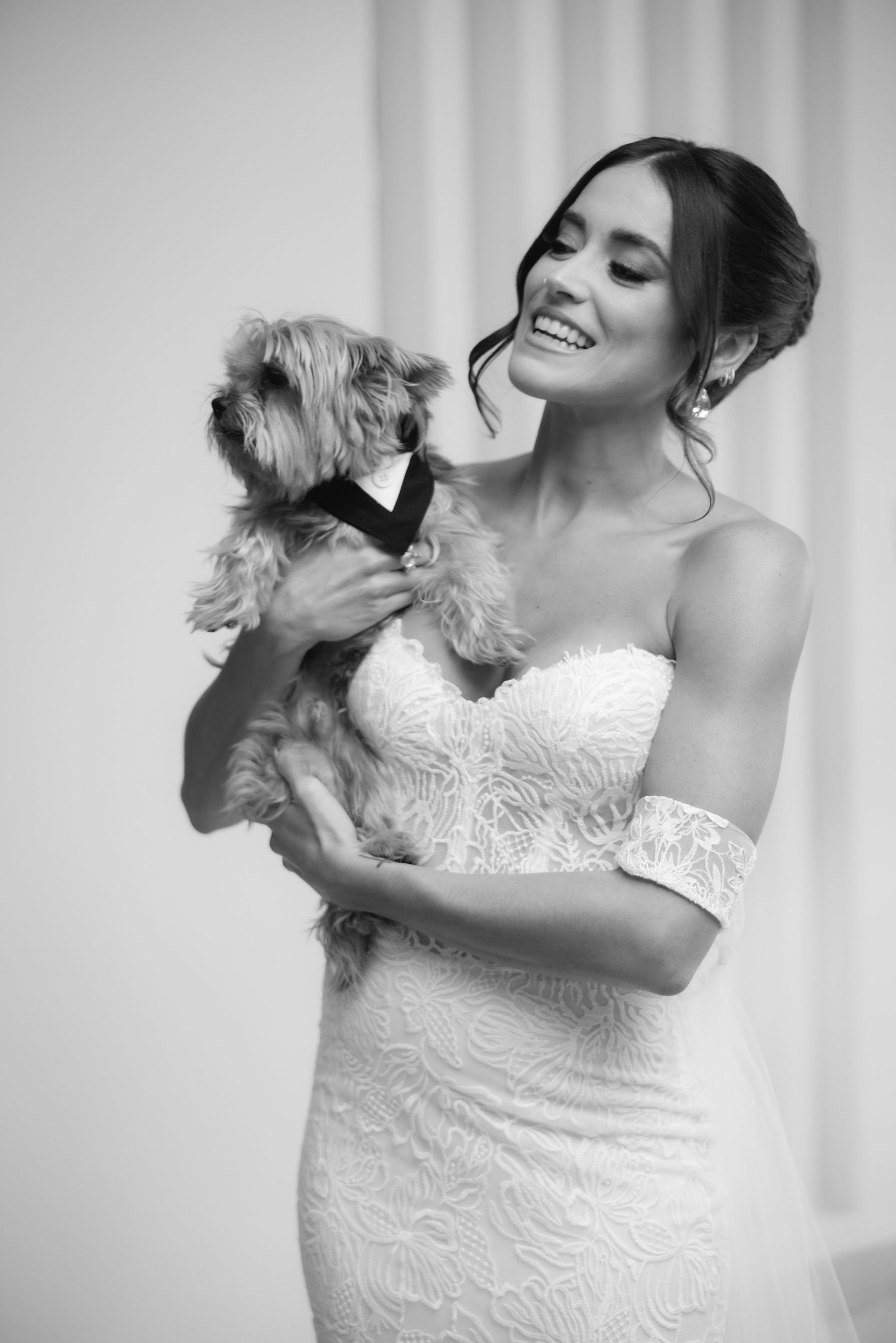 Sweet moment between a small dog in a bowtie and someone in a lace wedding dress.