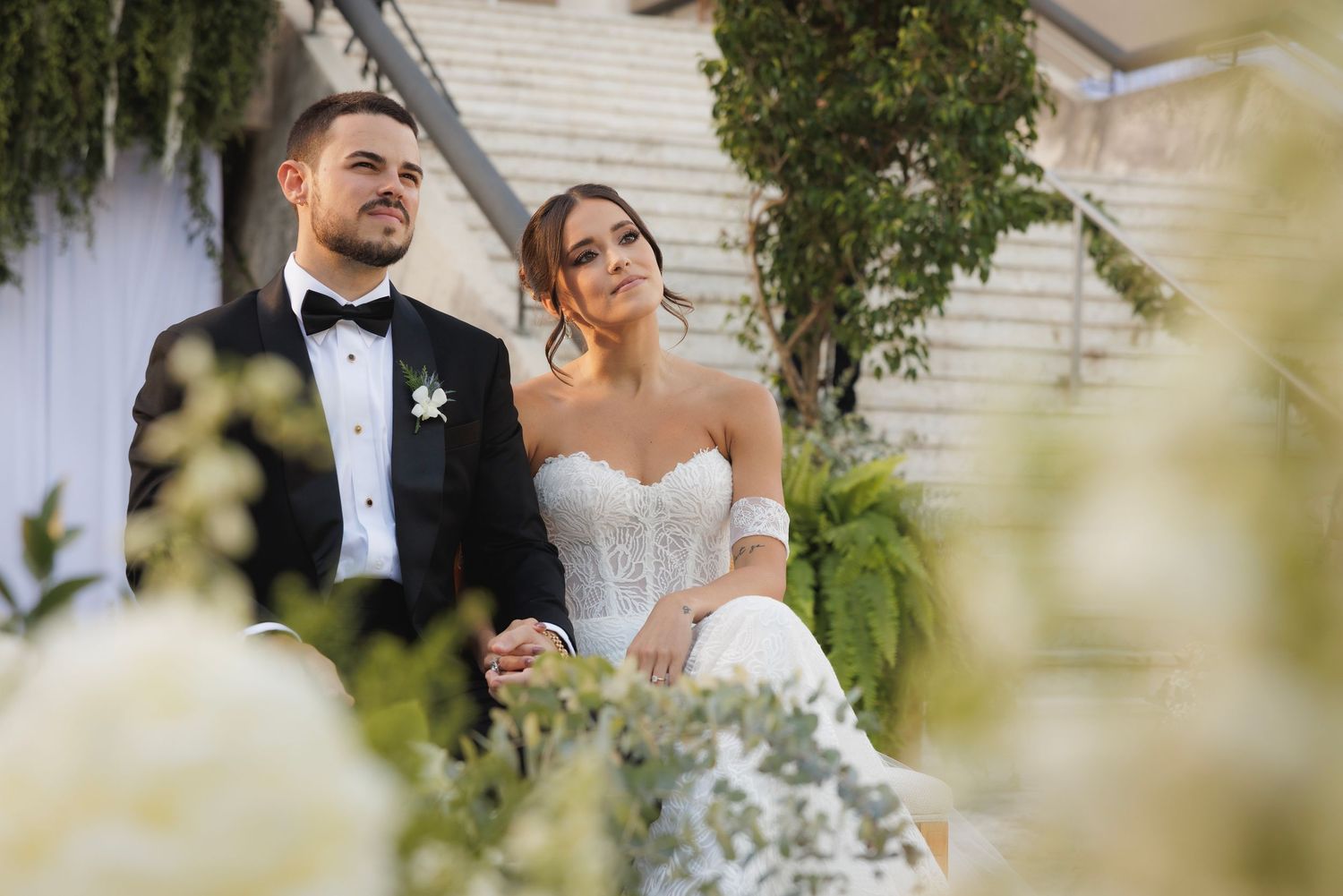 Newlywed couple shares an intimate outdoor moment surrounded by greenery and soft natural light.