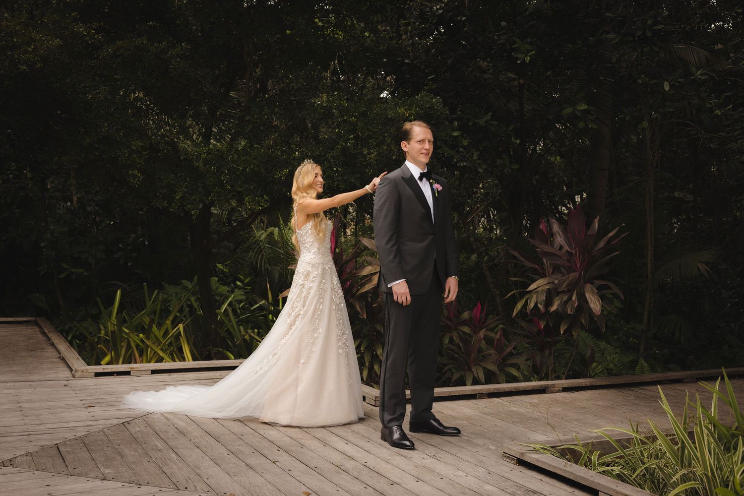 A romantic wedding photo shoot on a stone deck with tropical plants and trees in the background.