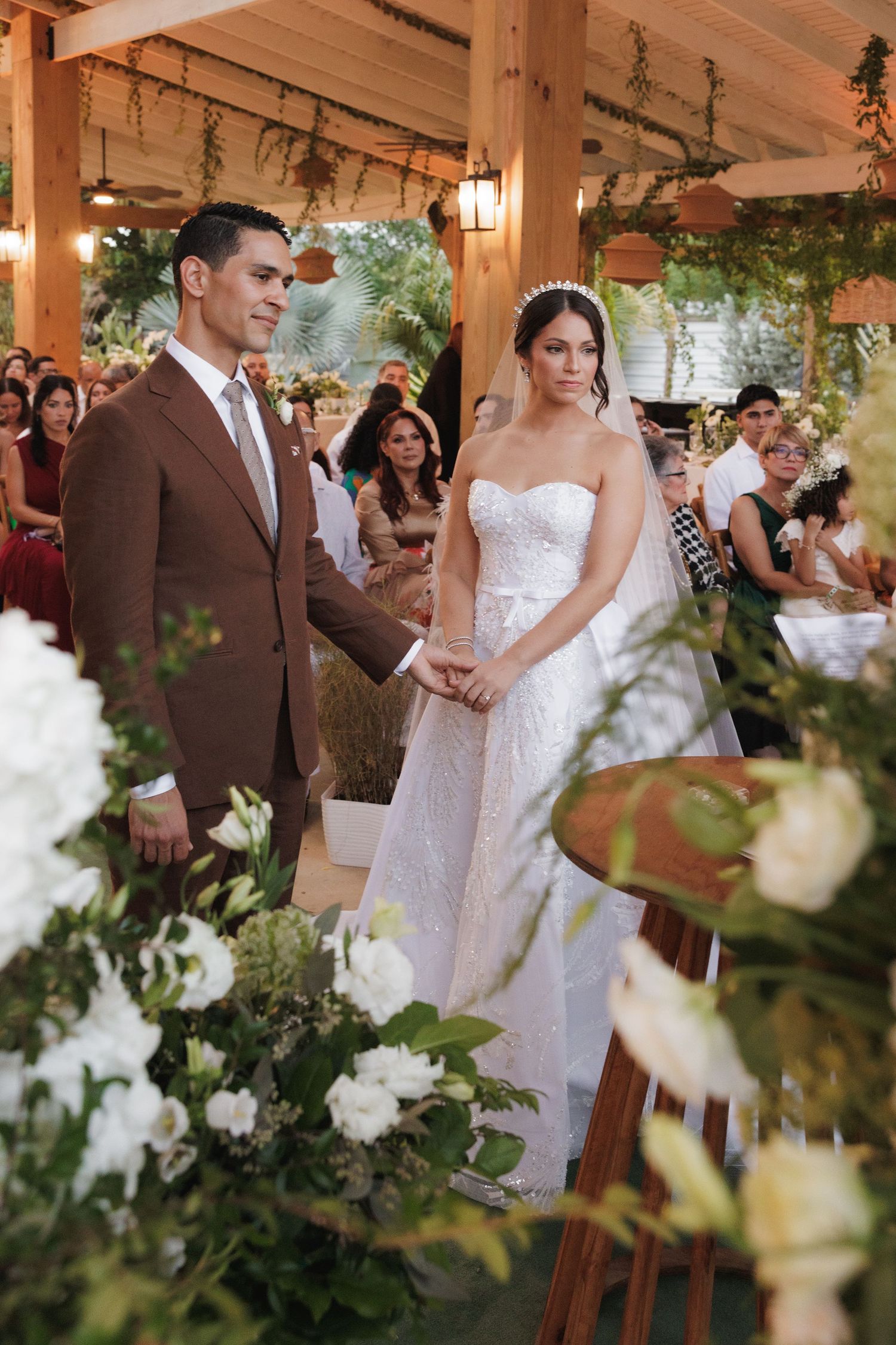 Wedding ceremony in a rustic wooden pavilion decorated with greenery and white flowers.