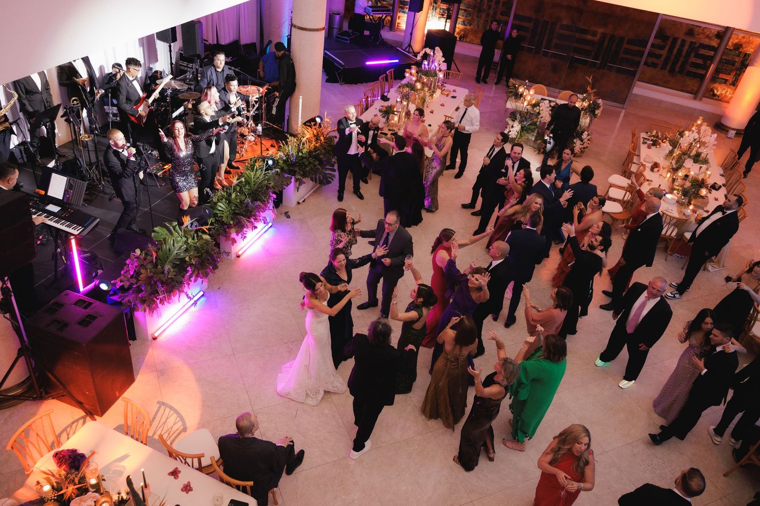 Overhead view of wedding guests mingling and dancing in a ballroom with purple lighting.