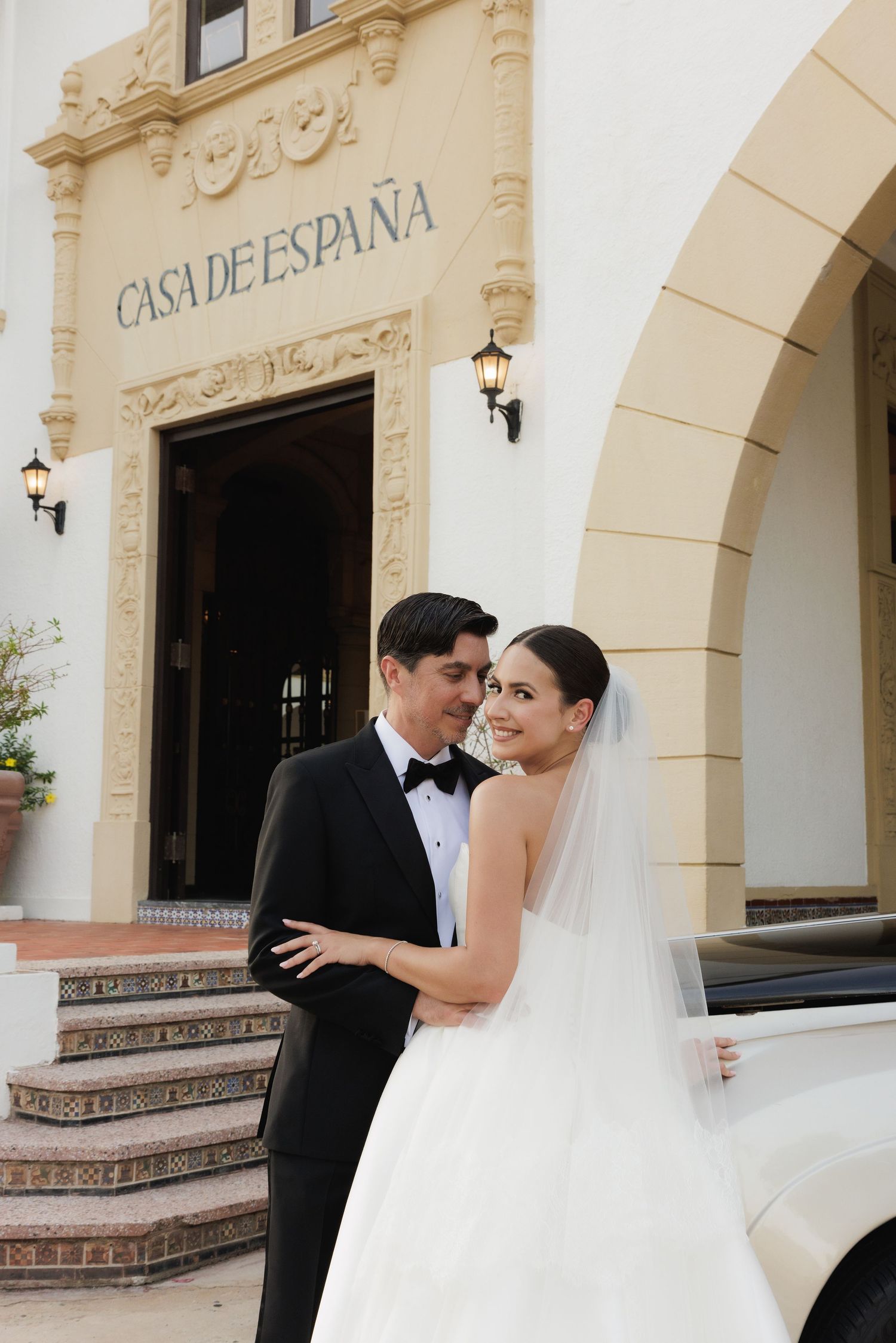 A wedding couple poses outside Casa de Espana, a Spanish-style building with ornate architectural details and wall sconces.