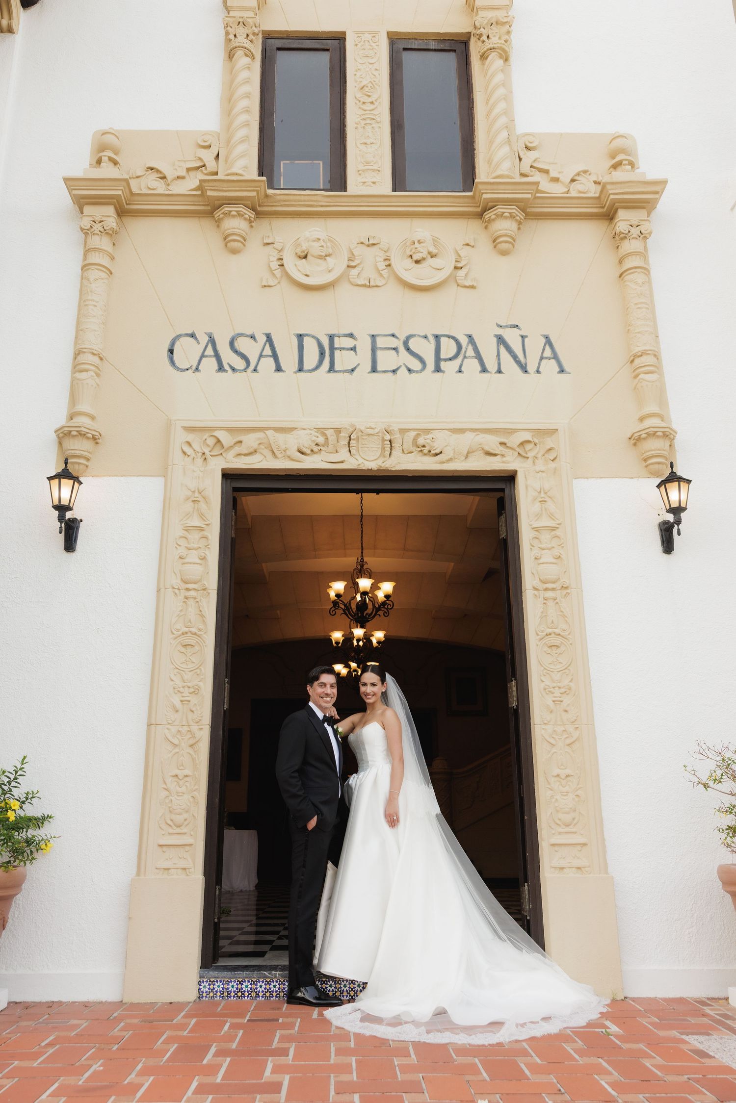 Elegant wedding couple posing at entrance of historic Casa de España building.