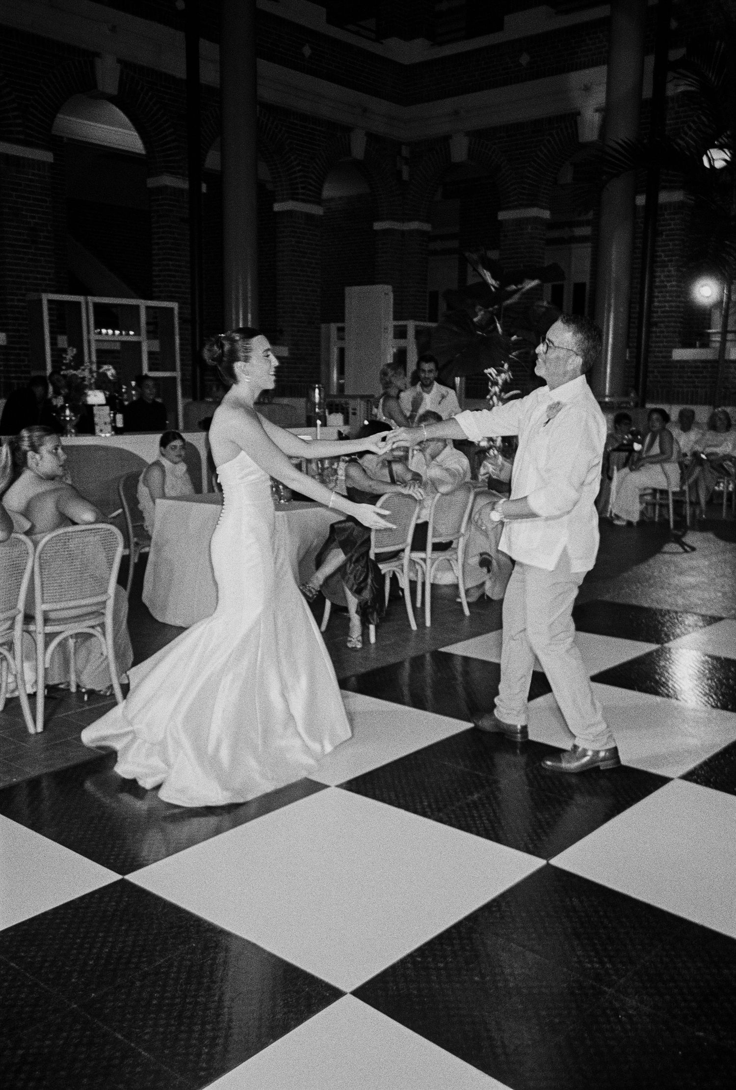 Bride and groom sharing a first dance on a black and white checkered dance floor at their wedding reception.