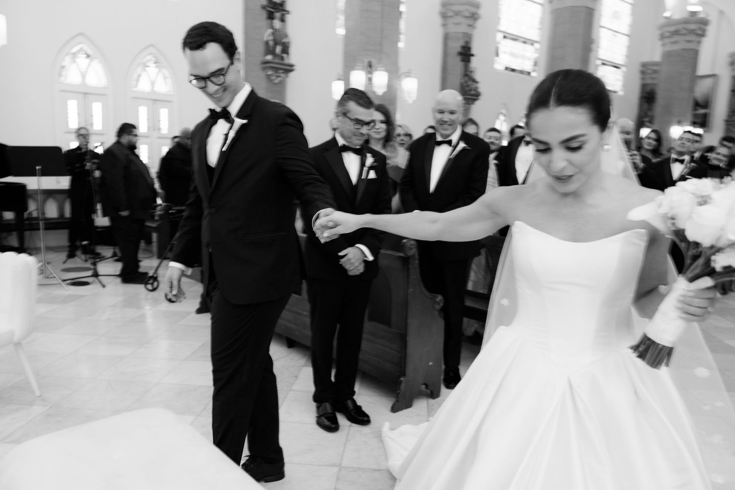 A black and white photo of a couple dancing during their wedding reception in a grand ballroom.