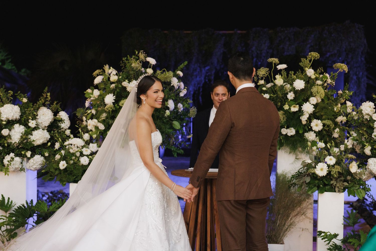 Romantic wedding ceremony setup with white floral arrangements and blue accent lighting.