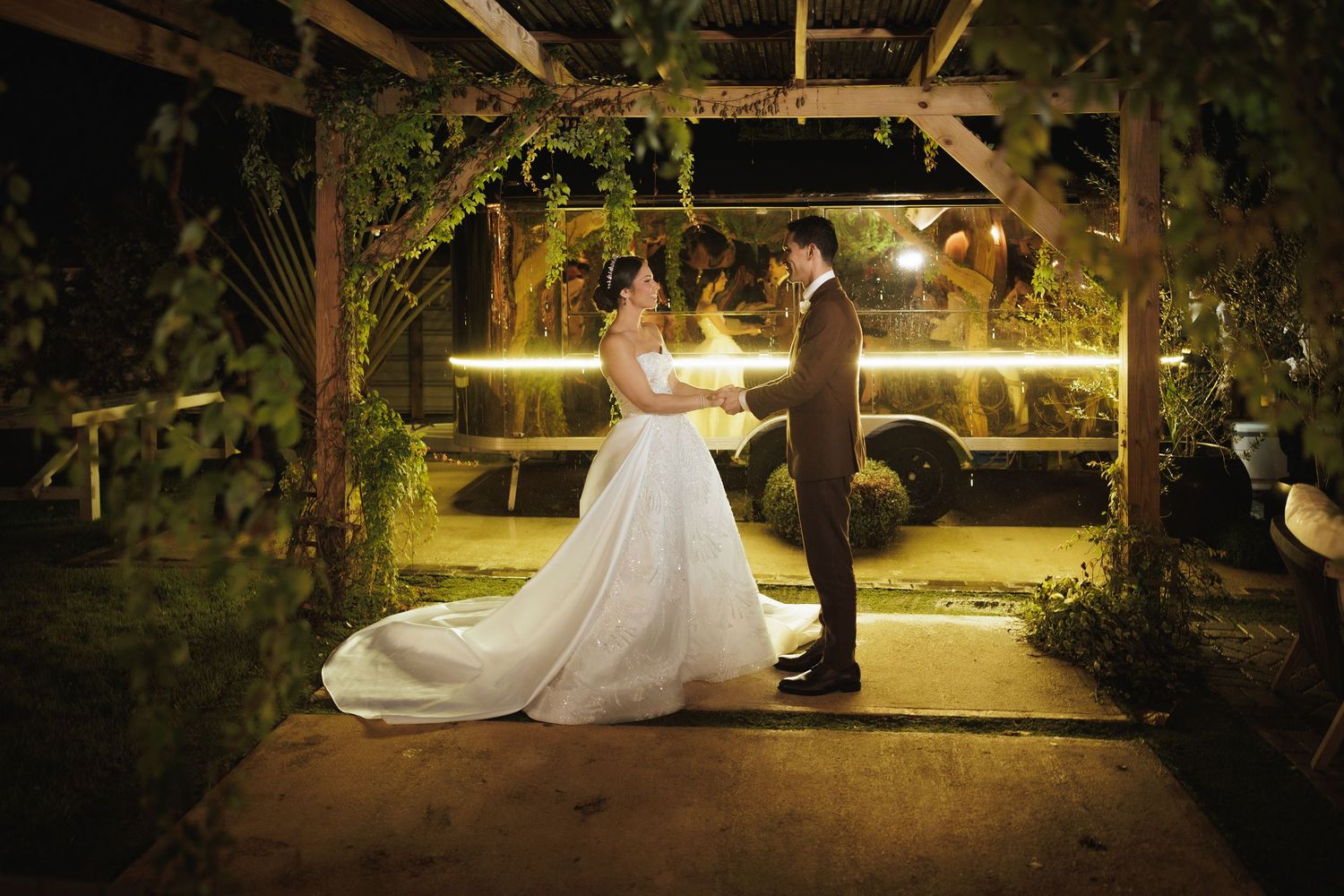 Romantic couple dancing together at night in an outdoor garden setting with glowing lights.
