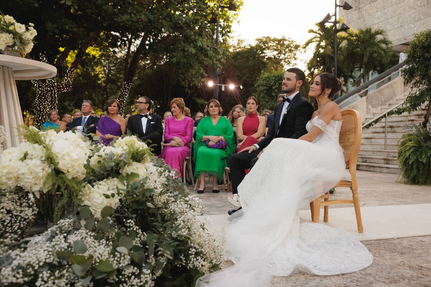 Elegant outdoor wedding ceremony setup with white floral arrangements and stone architecture.