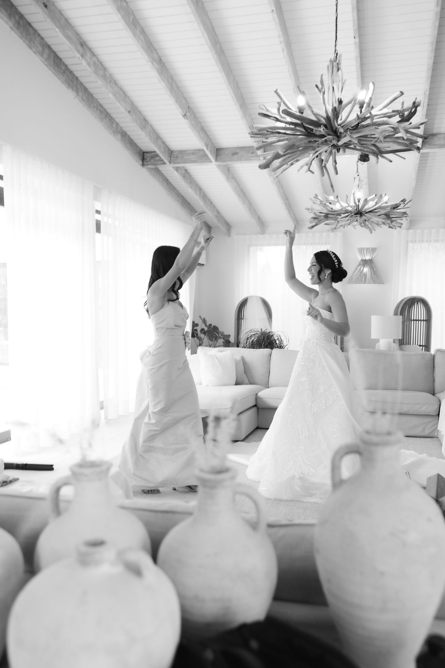 Two figures in white dresses dance joyfully in a bright room with decorative vases.