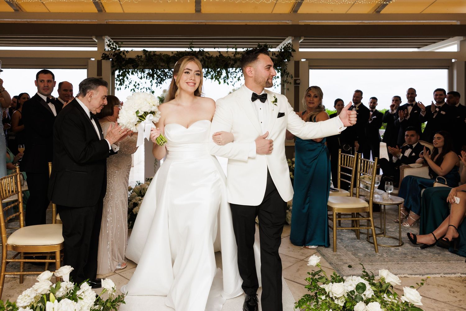 Wedding ceremony setup with white floral arrangements and guests seated under covered outdoor venue.
