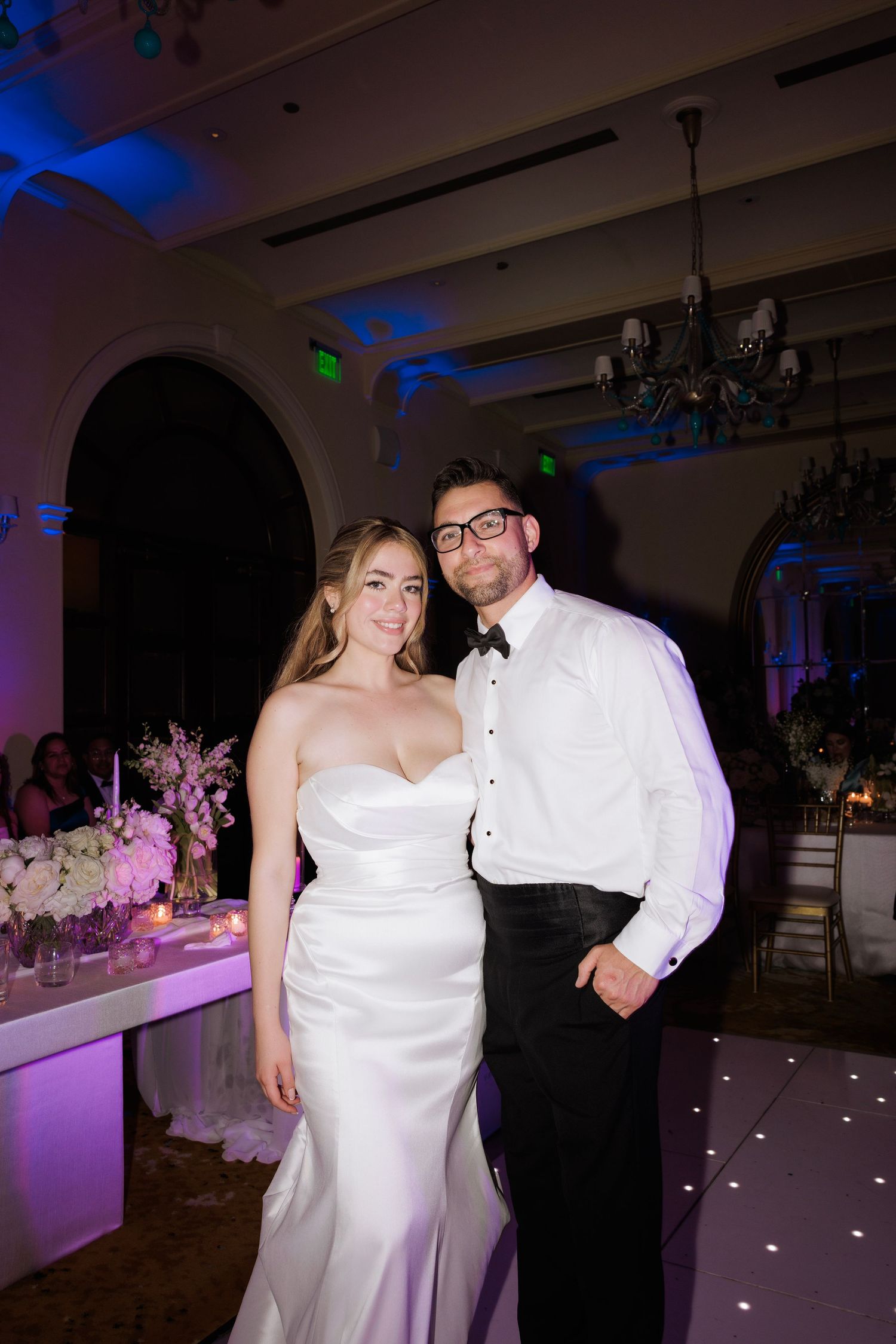 Couple dancing together under purple mood lighting at an elegant indoor reception.