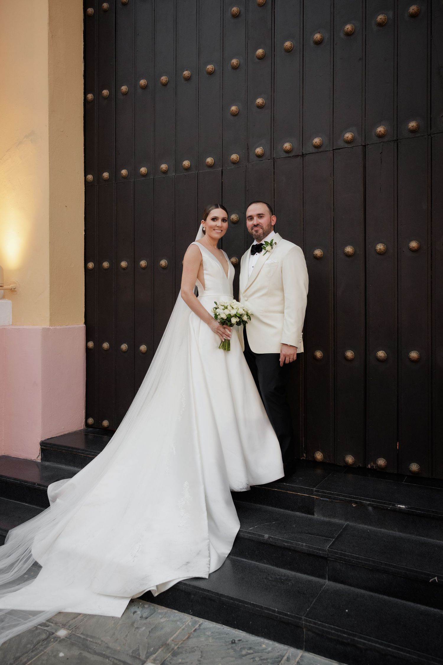 Elegant wedding portraits against ornate black wooden doors with decorative studs.