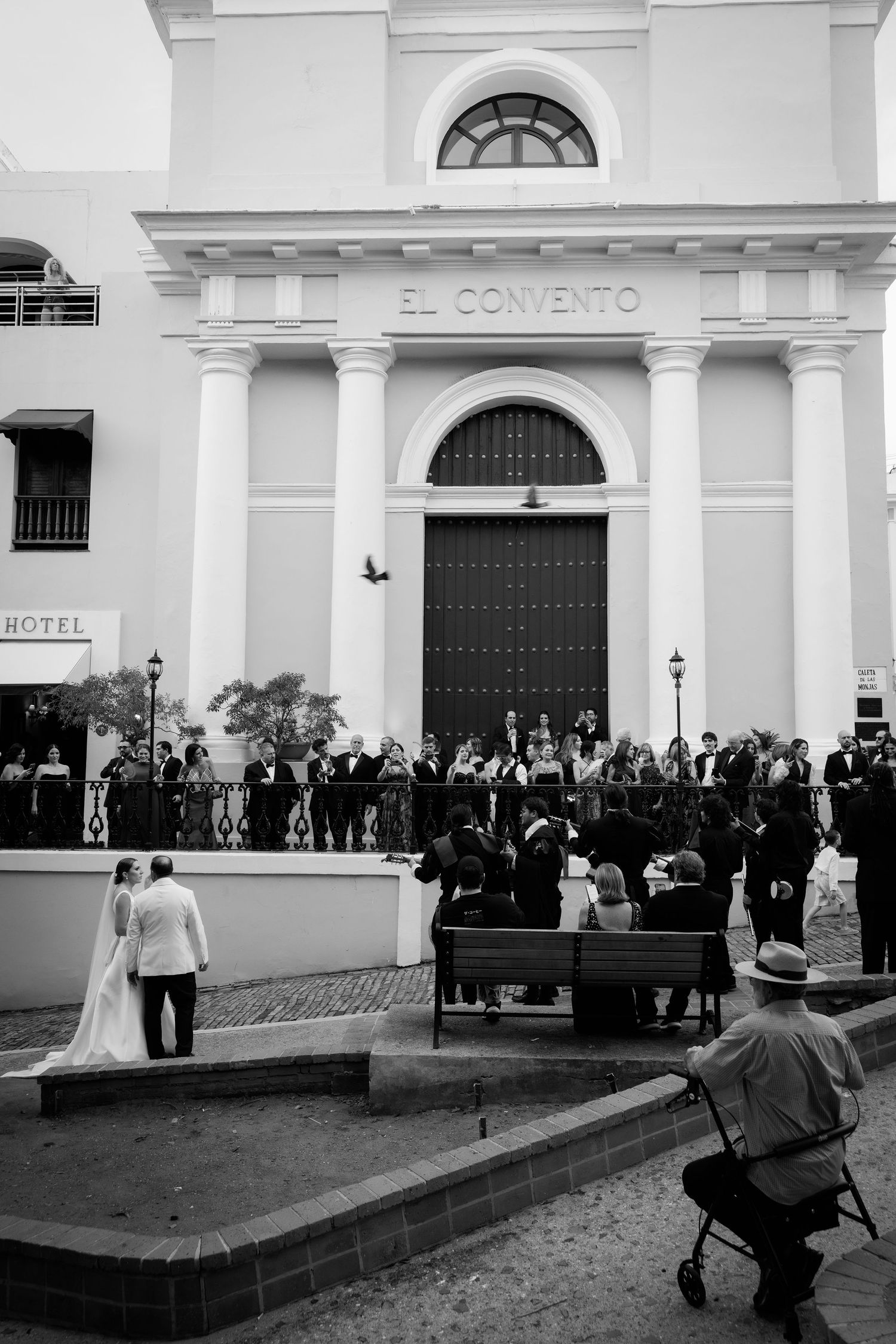 A black and white photo of a wedding ceremony outside El Convento hotel with guests watching.