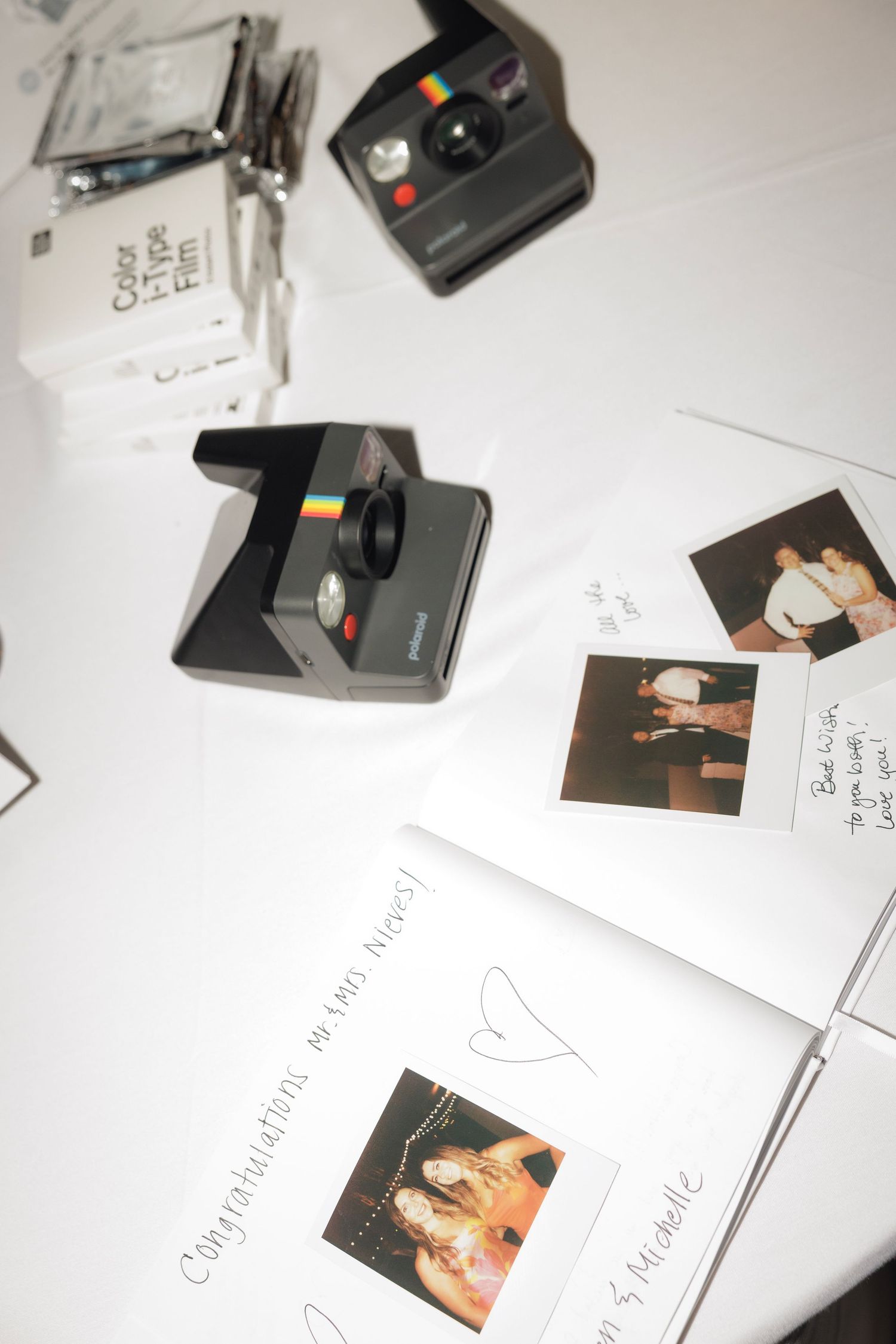 Polaroid cameras and instant photo prints arranged on a white surface with papers and notes.