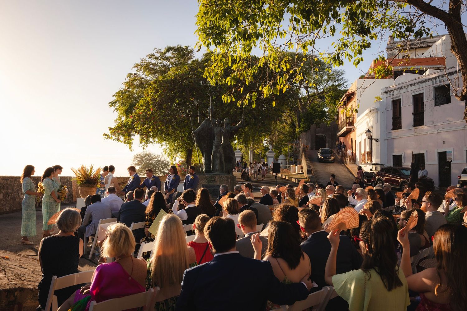 Wedding guests gather outdoors at dusk under trees for an evening celebration ceremony.