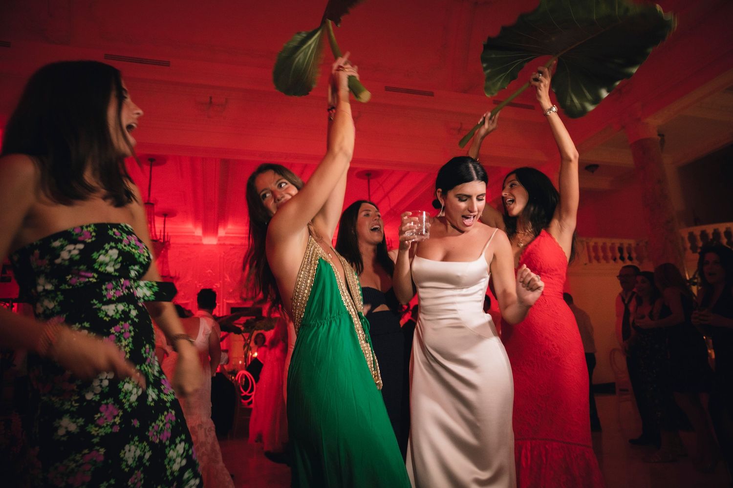 People dancing at a wedding reception with red mood lighting and festive atmosphere.