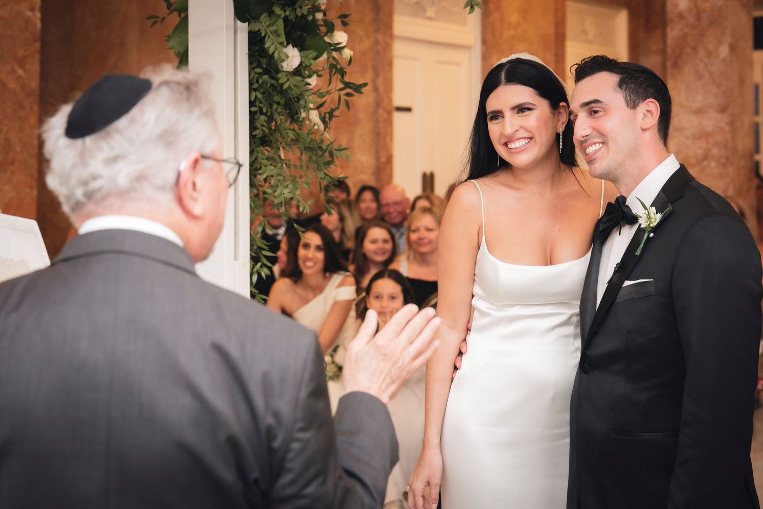 Wedding party celebrates with joyful dance moves during an indoor reception at an elegant venue.