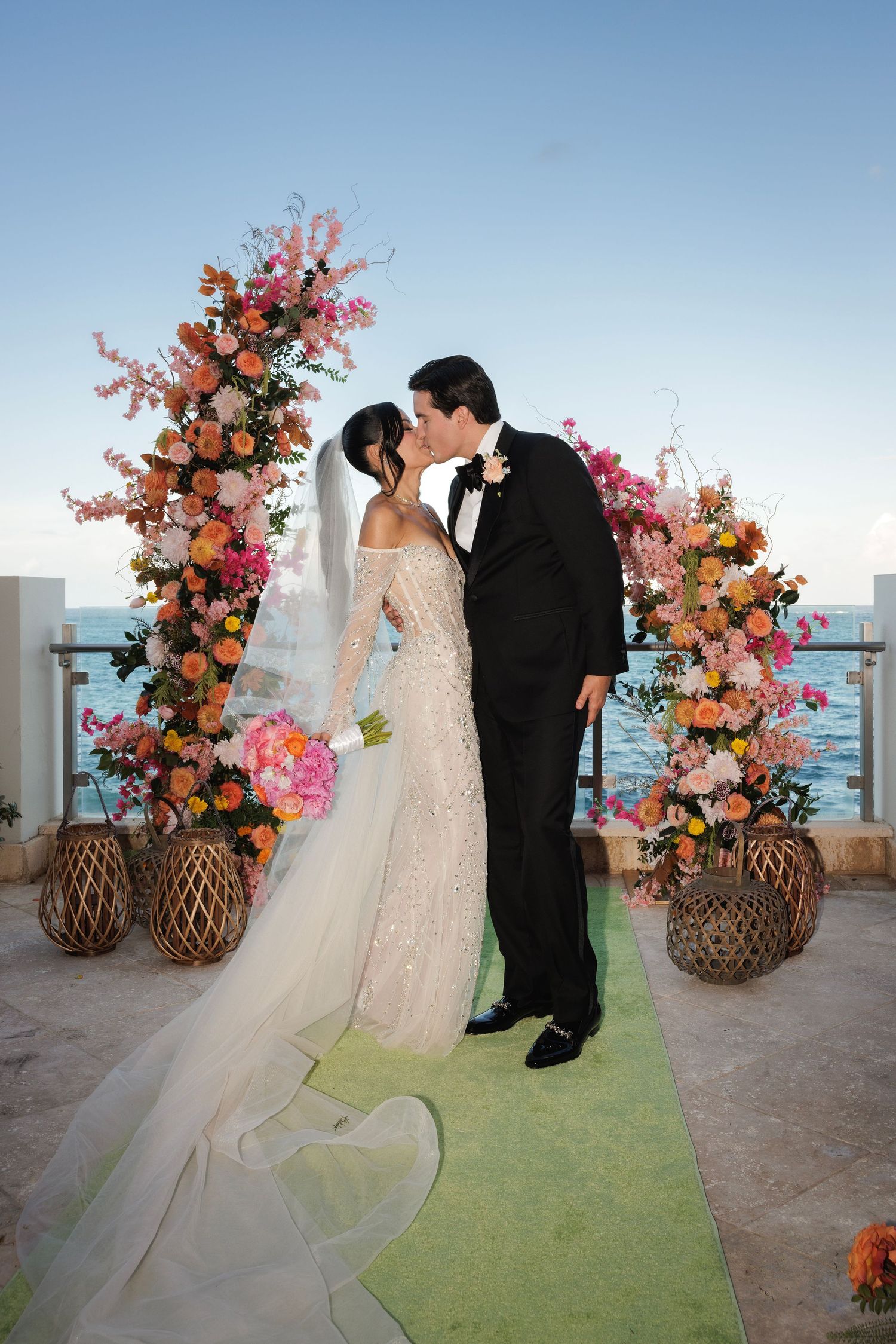 Romantic wedding ceremony on a rooftop with coral and pink floral arch decorations and lantern accents at sunset.