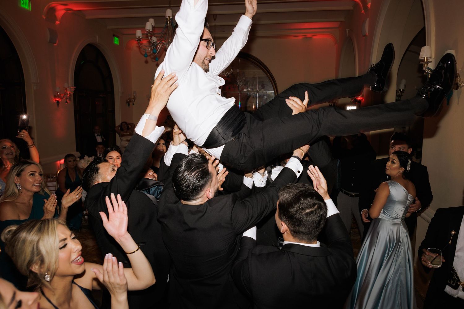 Wedding guests dancing energetically at a formal reception with dramatic red lighting effects.