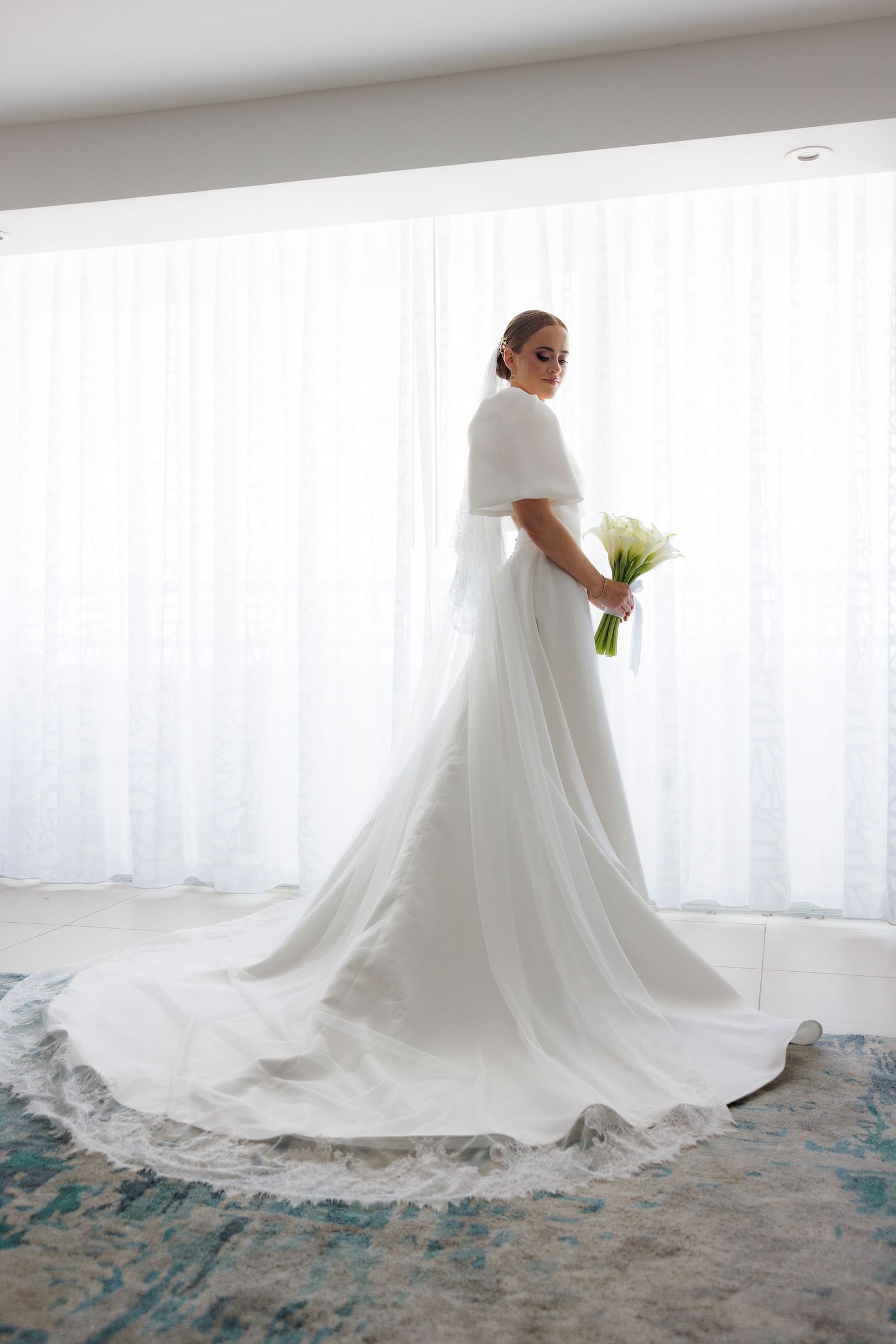 A flowing white wedding dress with a dramatic train sweeps across a blue-toned carpet.