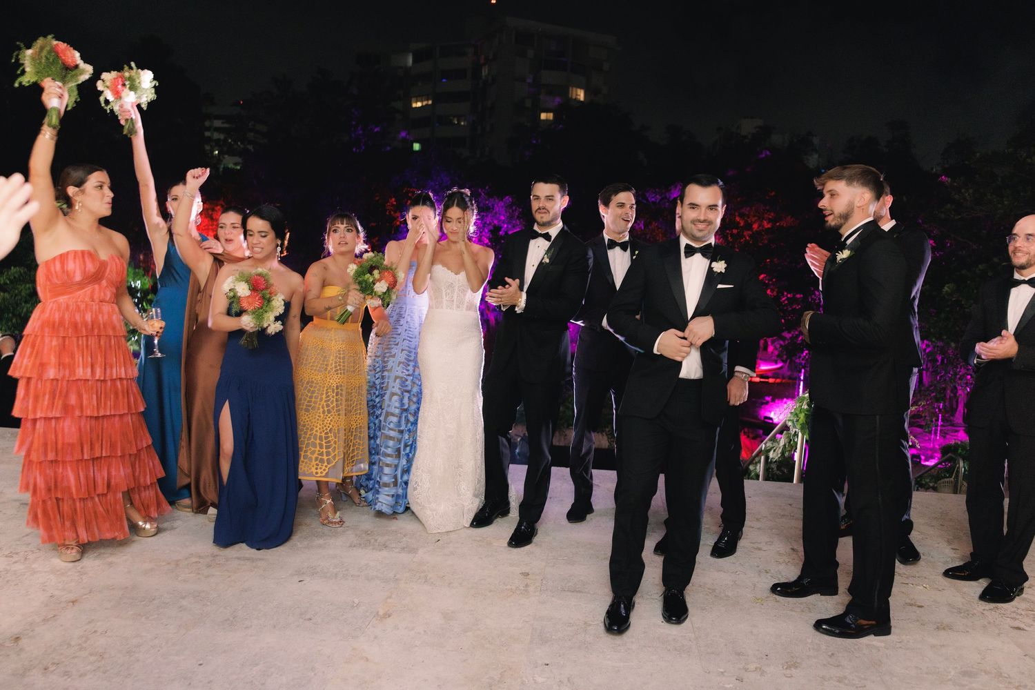 Formal event attendees in elegant evening wear stand together on a dance floor during an upscale celebration.