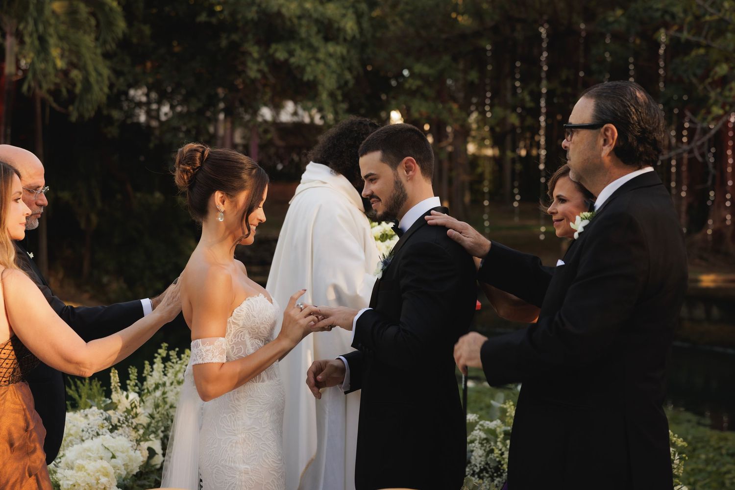 A joyful wedding ceremony takes place outdoors in a garden setting during golden hour.