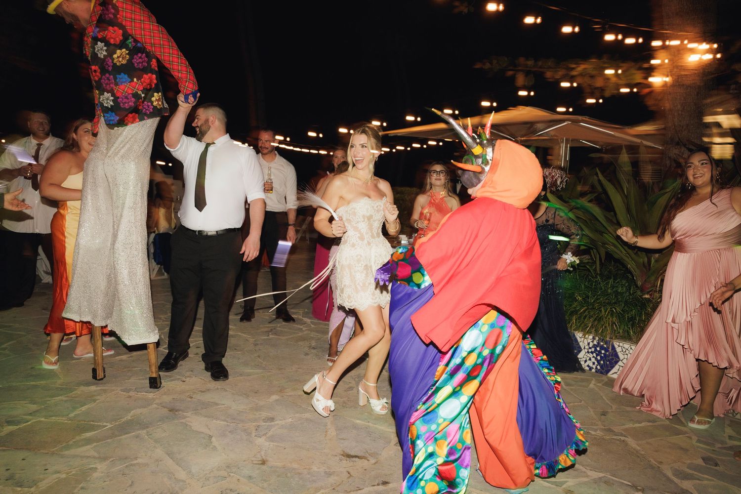 Wedding guests dance enthusiastically on an outdoor patio during an evening celebration.