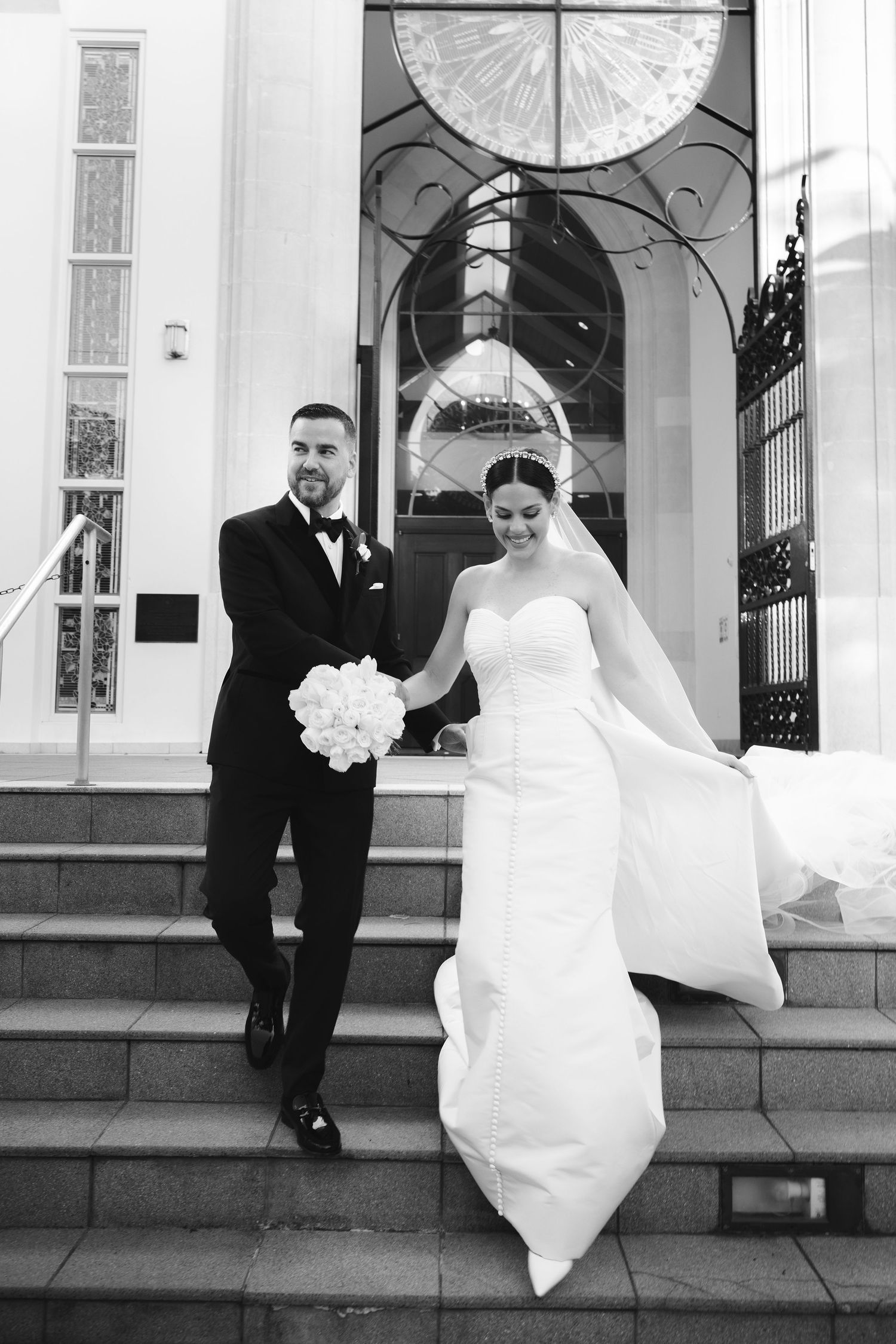 Five black and white wedding photos show a couple in traditional attire posing playfully outside a church entrance.