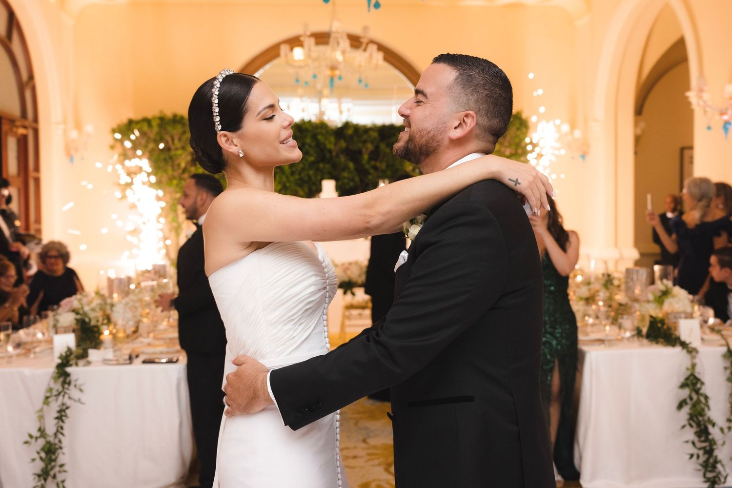 A romantic first dance at an elegant wedding reception with sparklers and floral decor in the background.