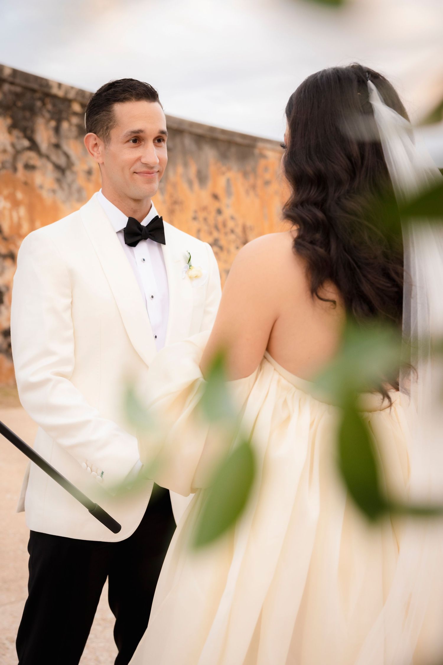 Elegant couple in formal attire photographed against warm terracotta walls.