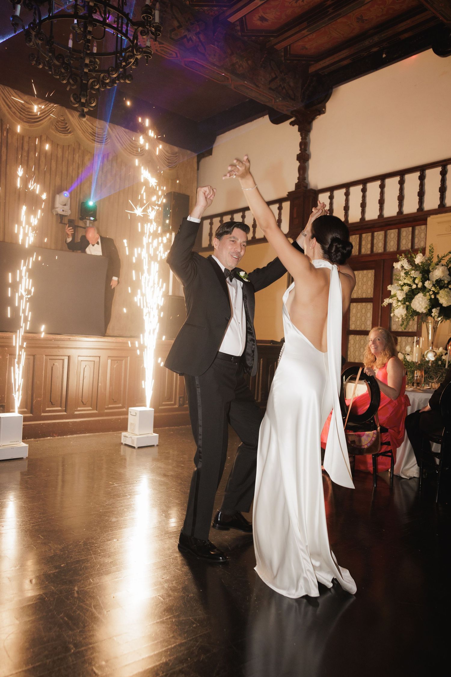 A couple dancing at their wedding reception with sparklers and dramatic lighting in an elegant venue.