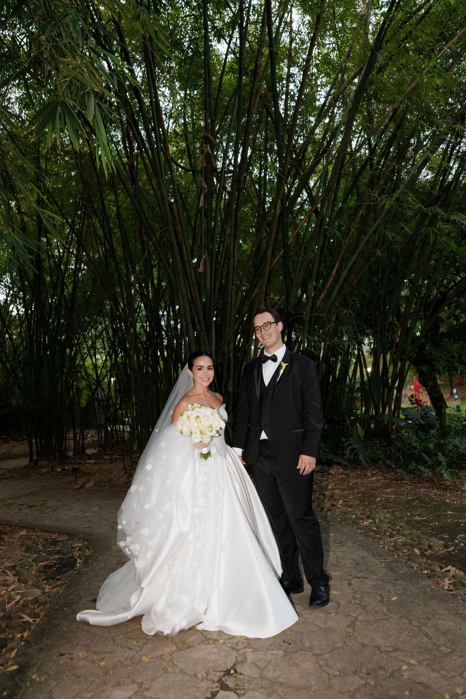 A bride and groom walk through a lush bamboo garden path during their wedding photo session.