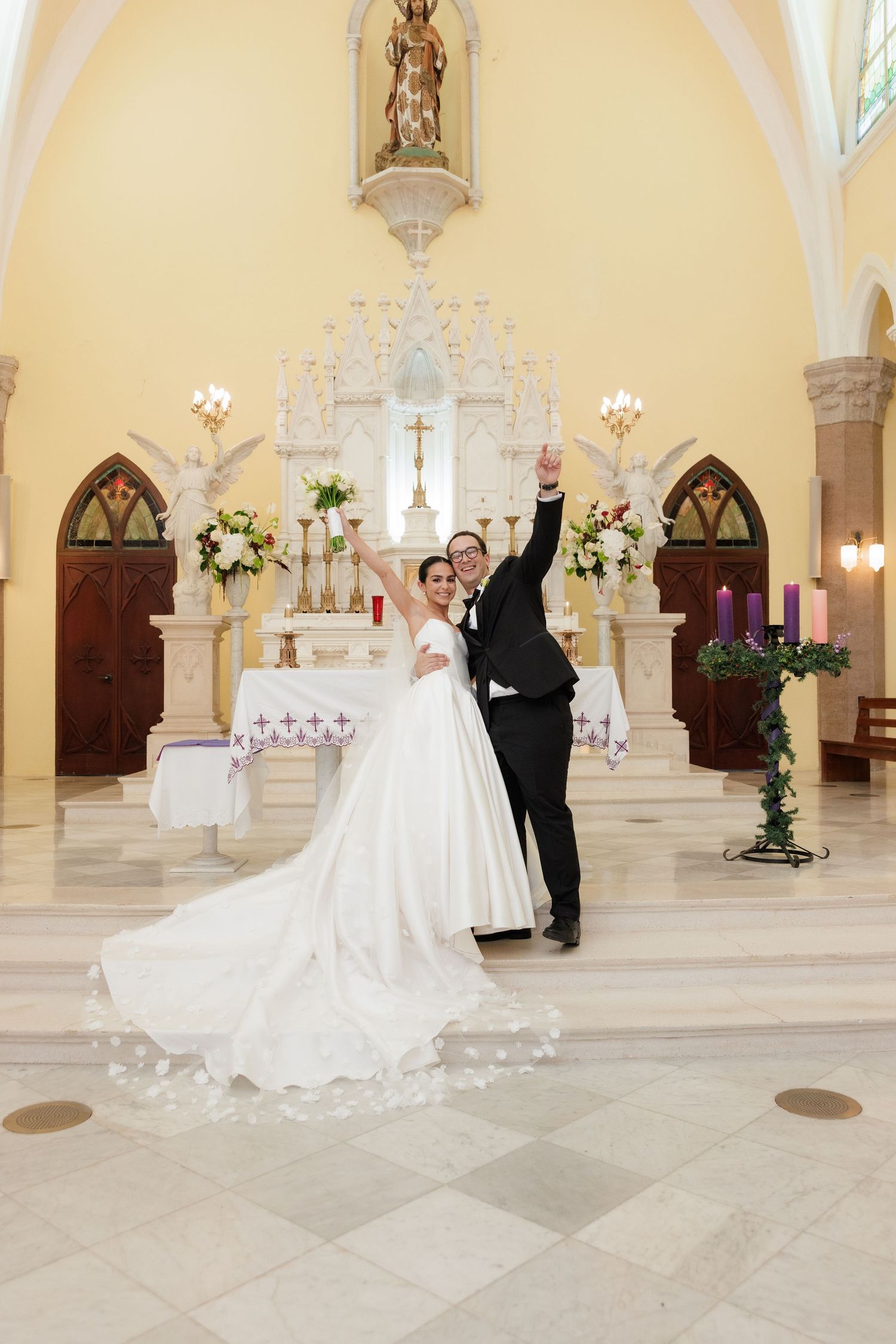 A wedding ceremony in a grand church interior with yellow walls, crystal chandeliers, and gothic arched windows.