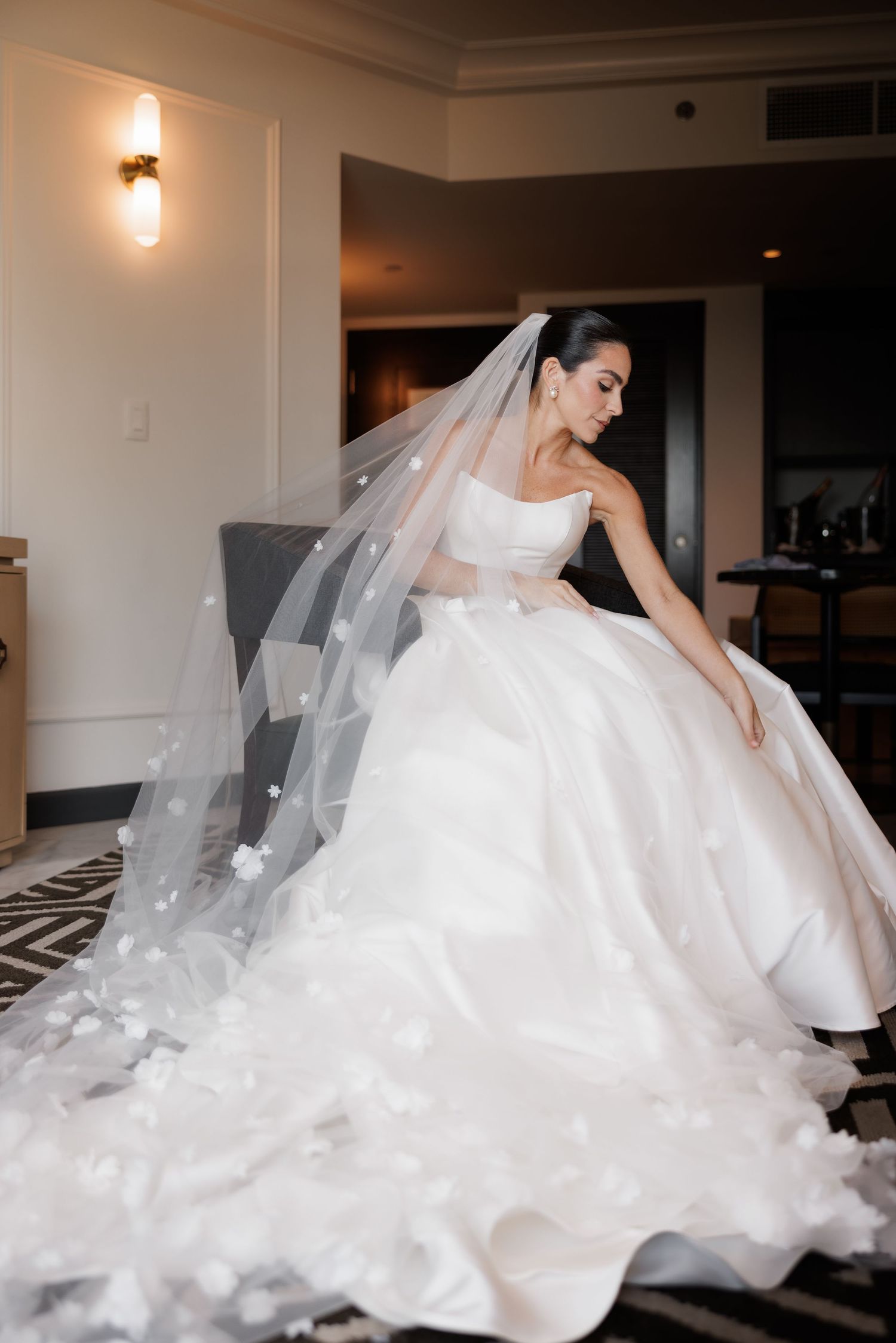 A bride in a voluminous white ballgown poses gracefully in an indoor setting with soft lighting.