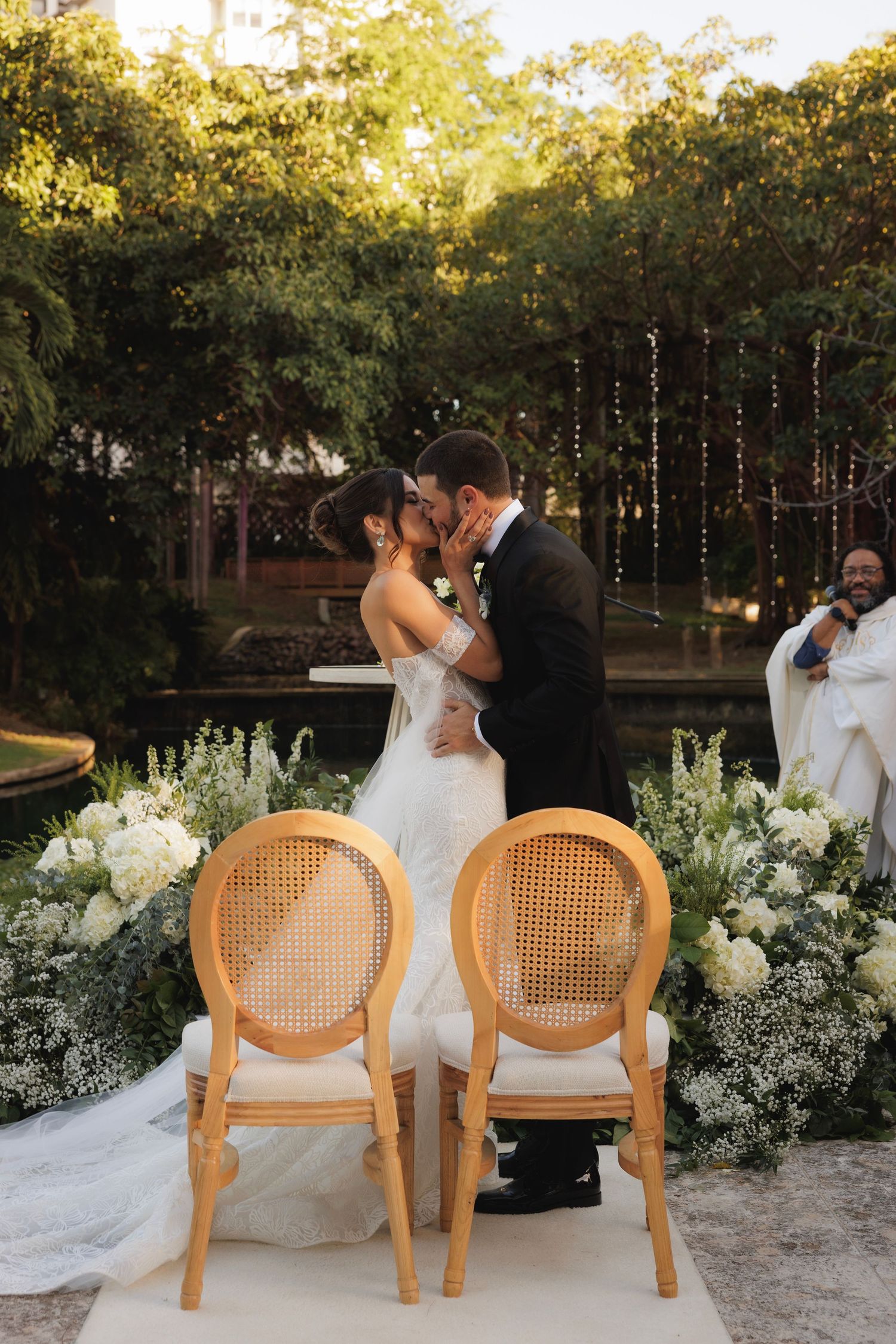 Two wooden cane chairs positioned outdoors near white floral arrangements at sunset.