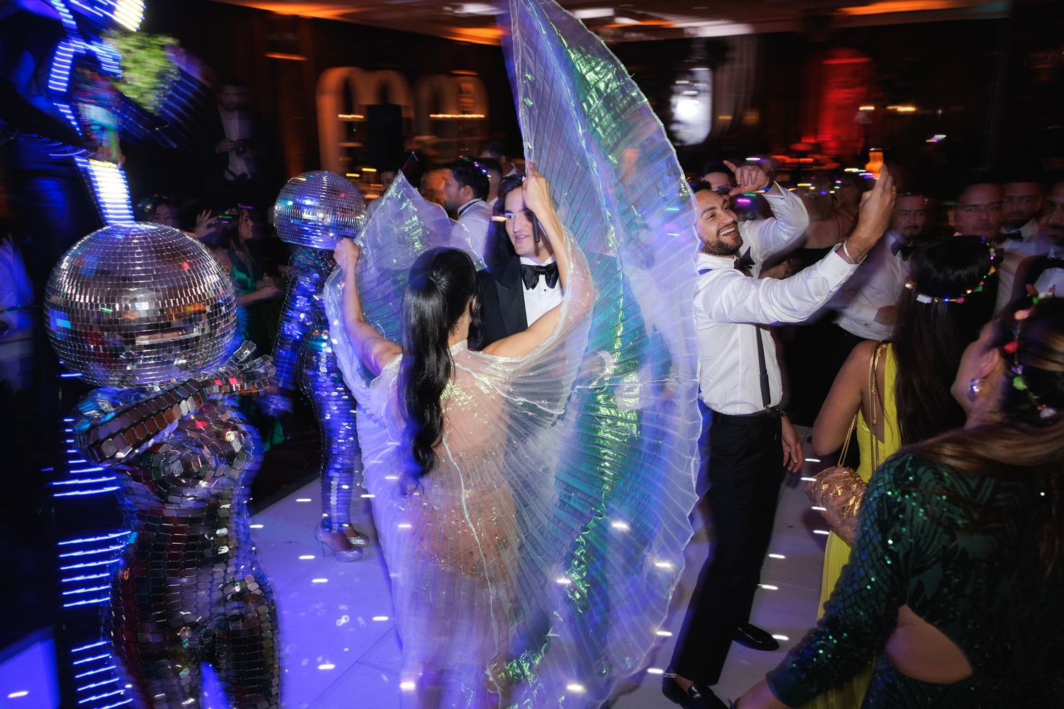 Dancers move beneath blue lighting and colorful effects at a nightclub party event.