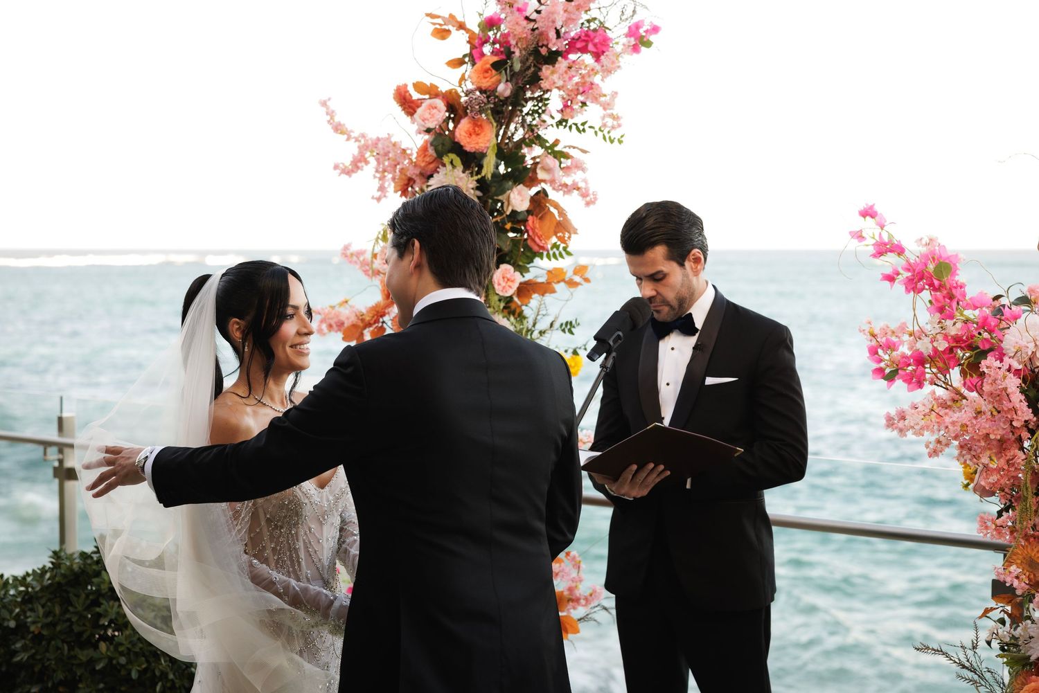 A seaside wedding ceremony with pink and peach floral arrangements by the ocean.