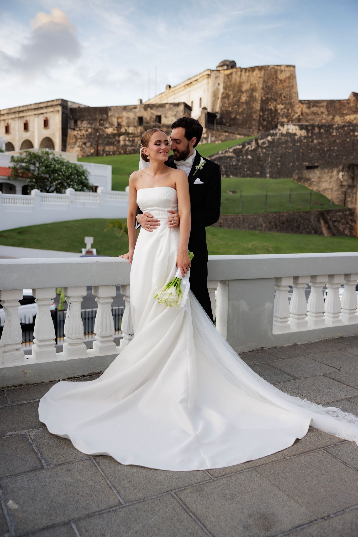A stunning wedding photo captured at a historic fortress with a dramatic flowing white gown against stone architecture.