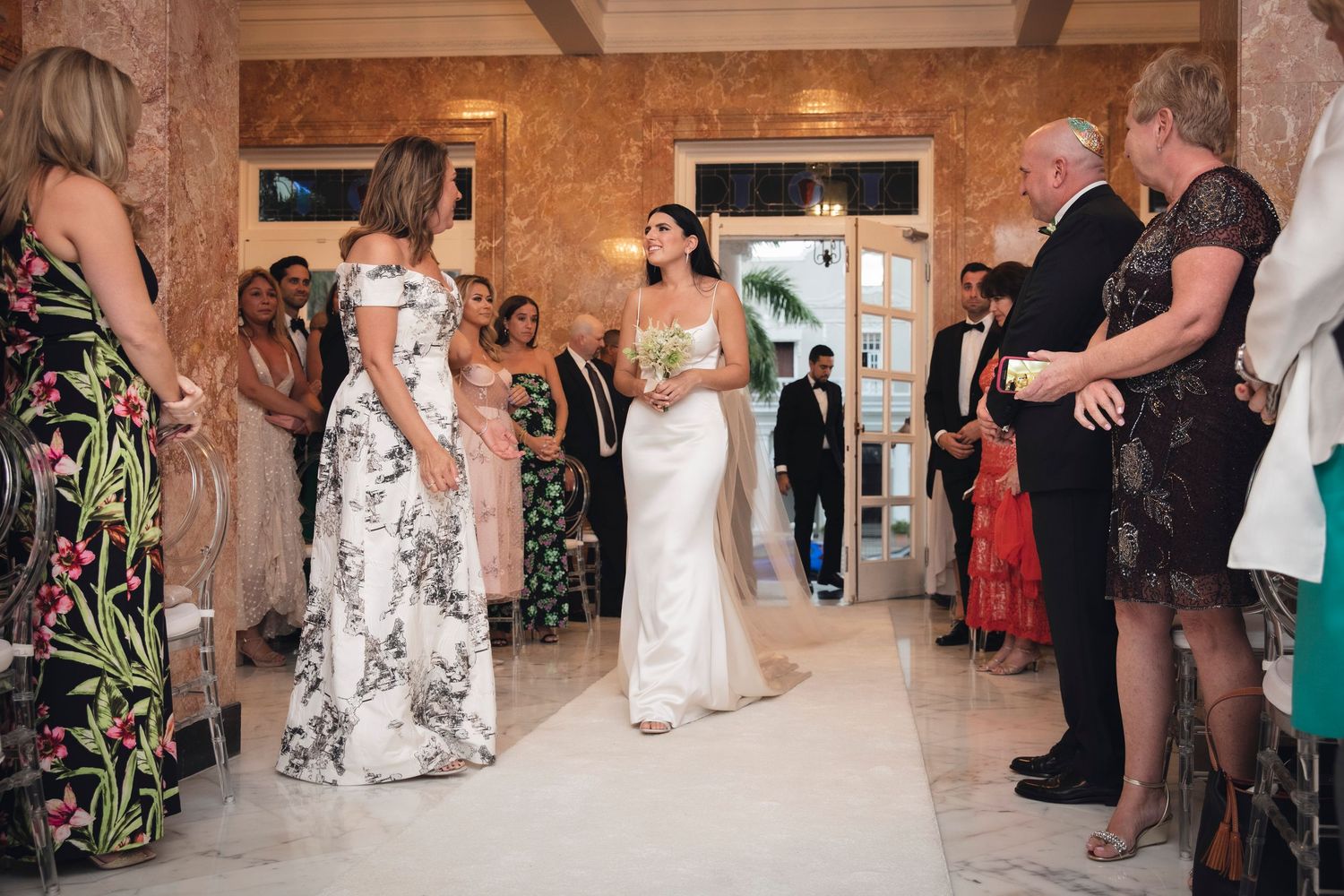Wedding guests watch as couples dance during an elegant reception in a rustic venue with wooden beams.
