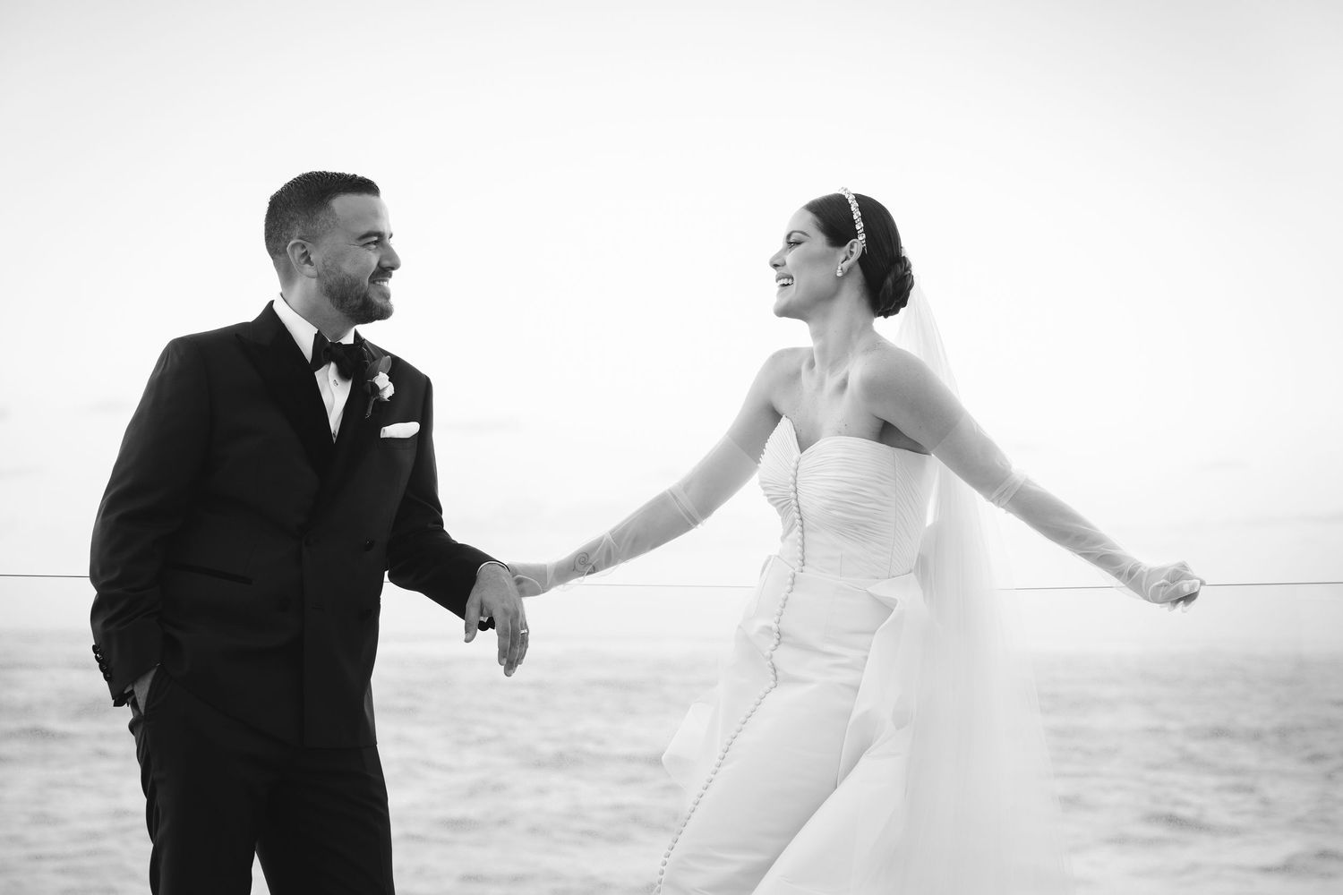 Black and white photo of a joyful wedding couple laughing together on a beach.