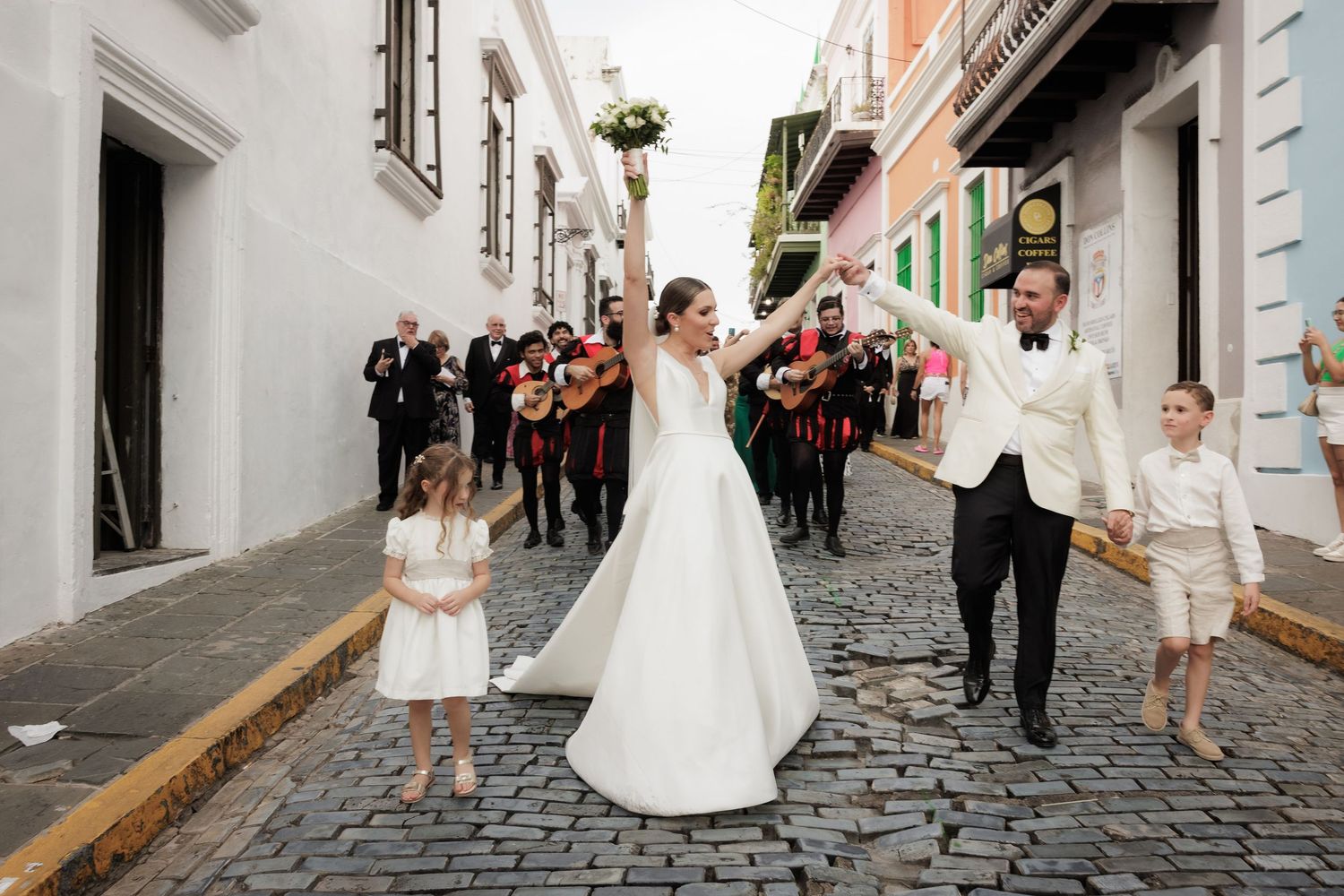 Wedding party walking down cobblestone street with flowing white dress.