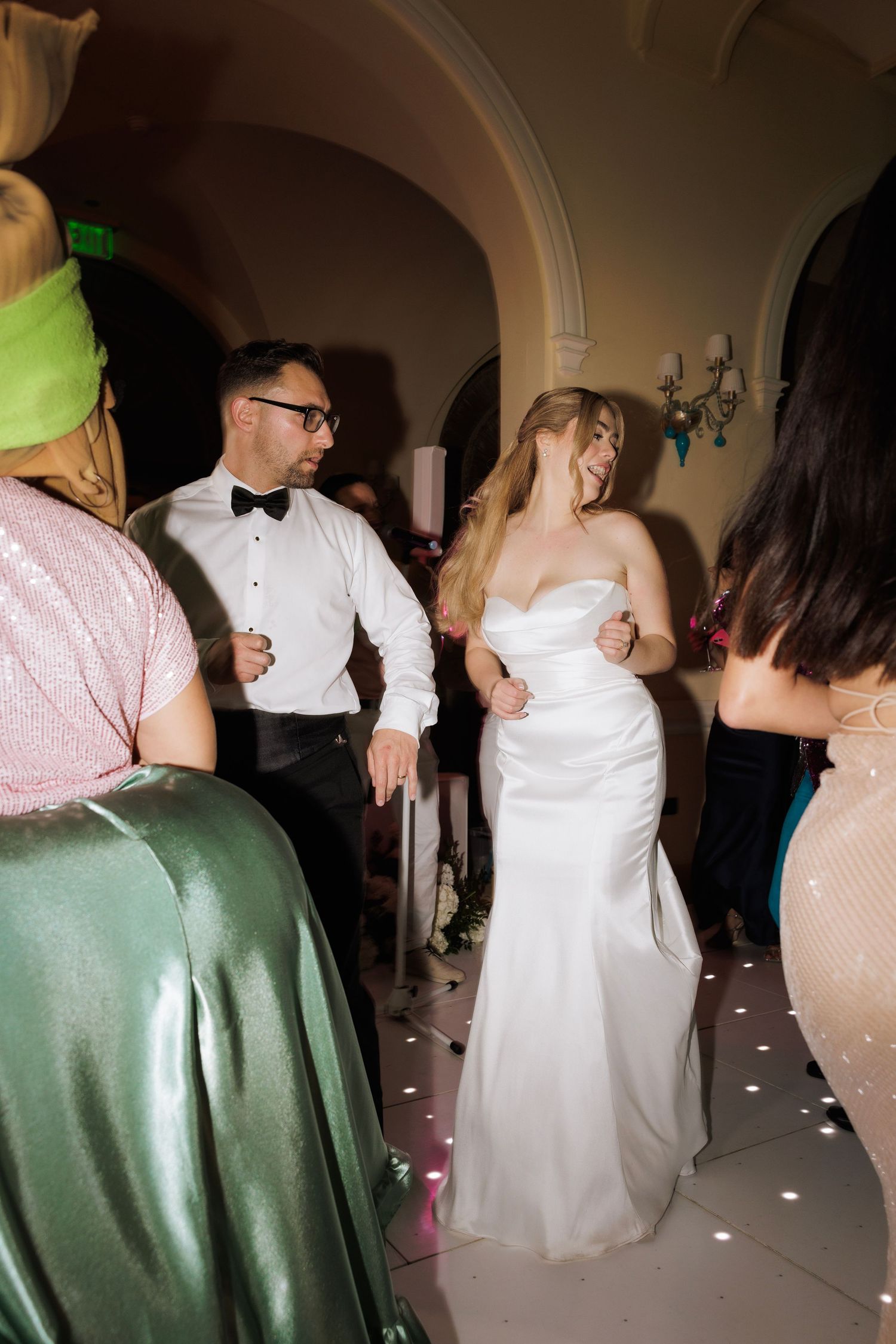Wedding celebration on a dance floor with guests in formal attire dancing and mingling.