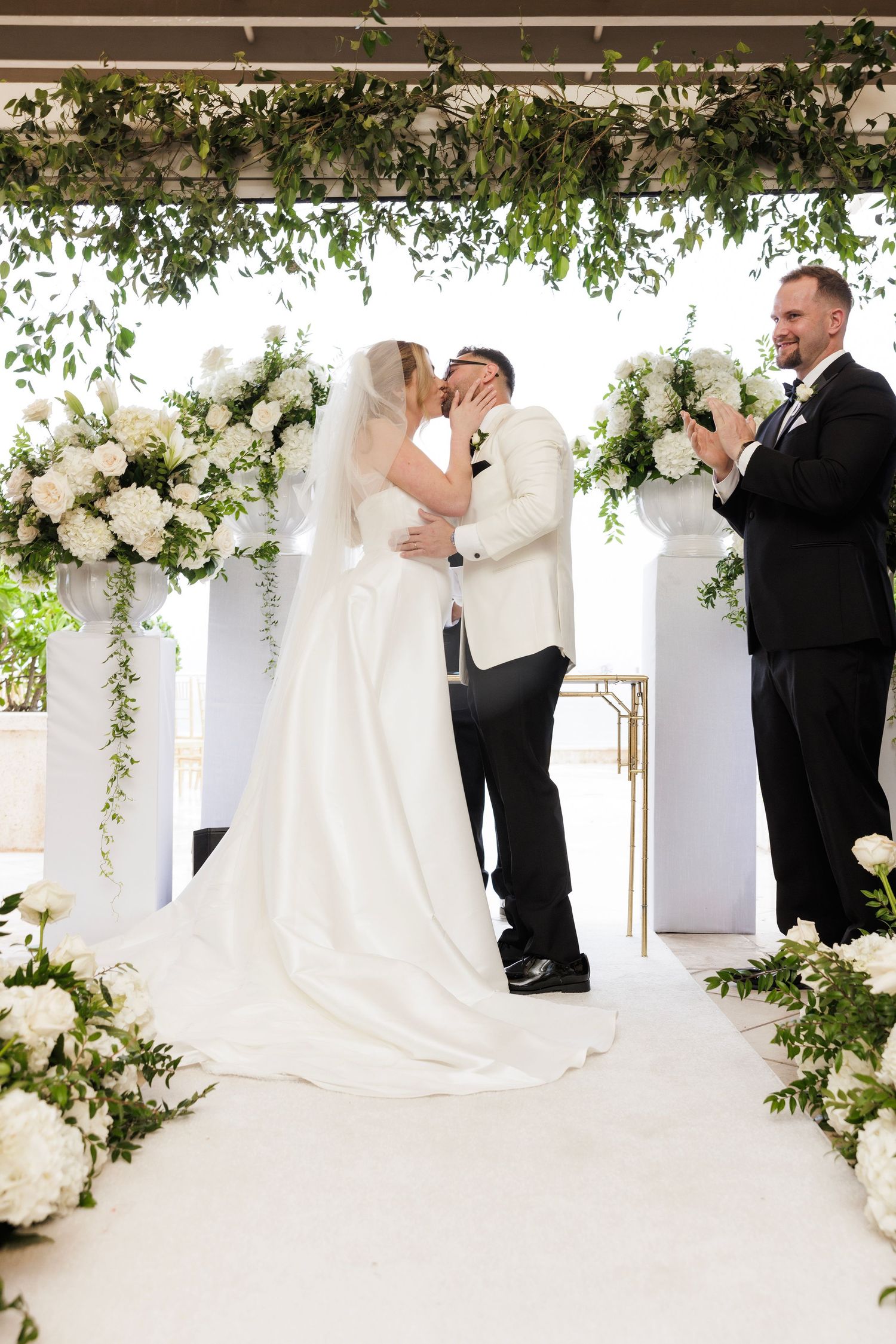 Wedding ceremony sequence under a decorated pergola with white flowers and cascading greenery.